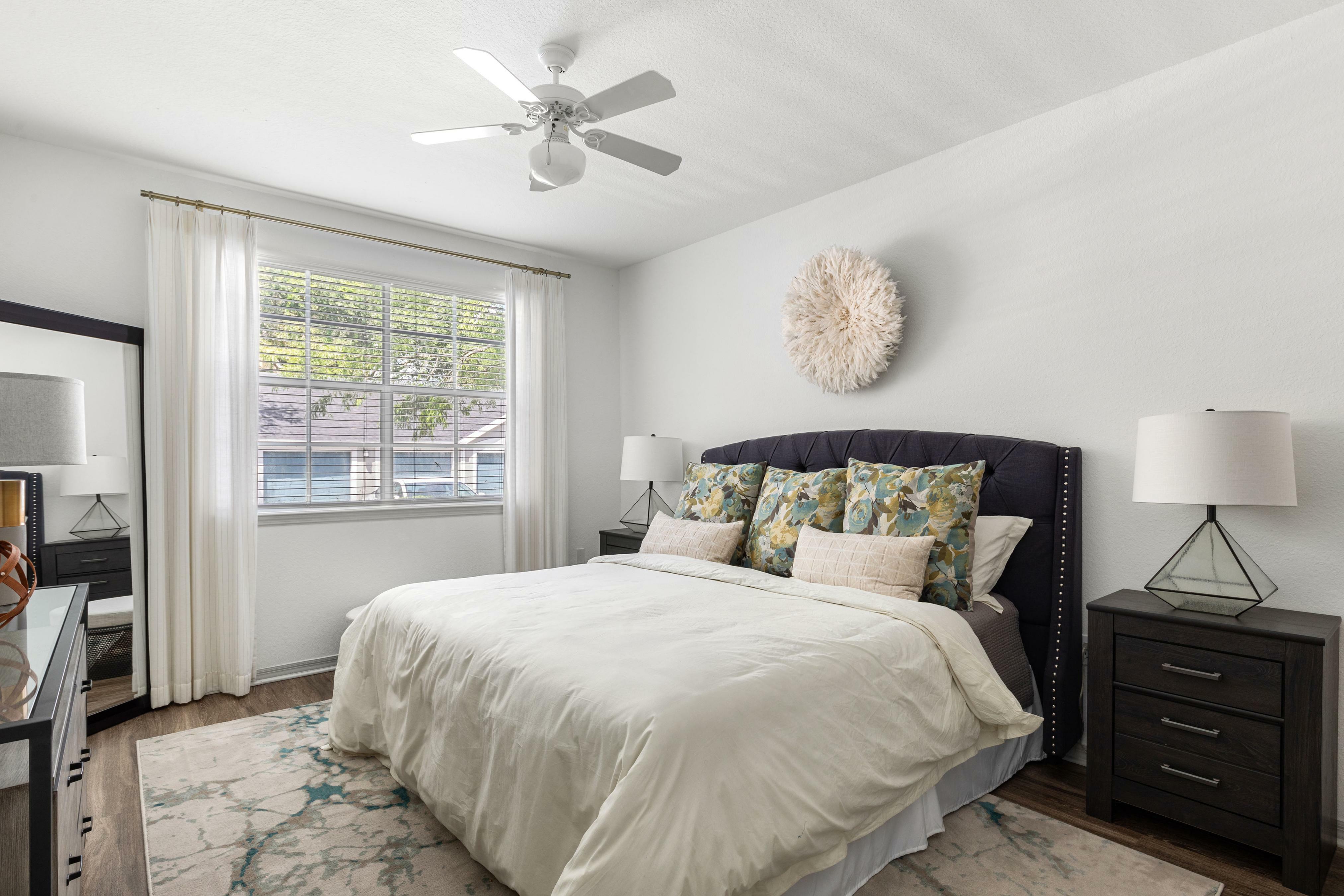 Bright and airy bedroom featuring a plush bed with decorative pillows, elegant nightstands, and large window draped with sheer curtains, offering a tranquil retreat.