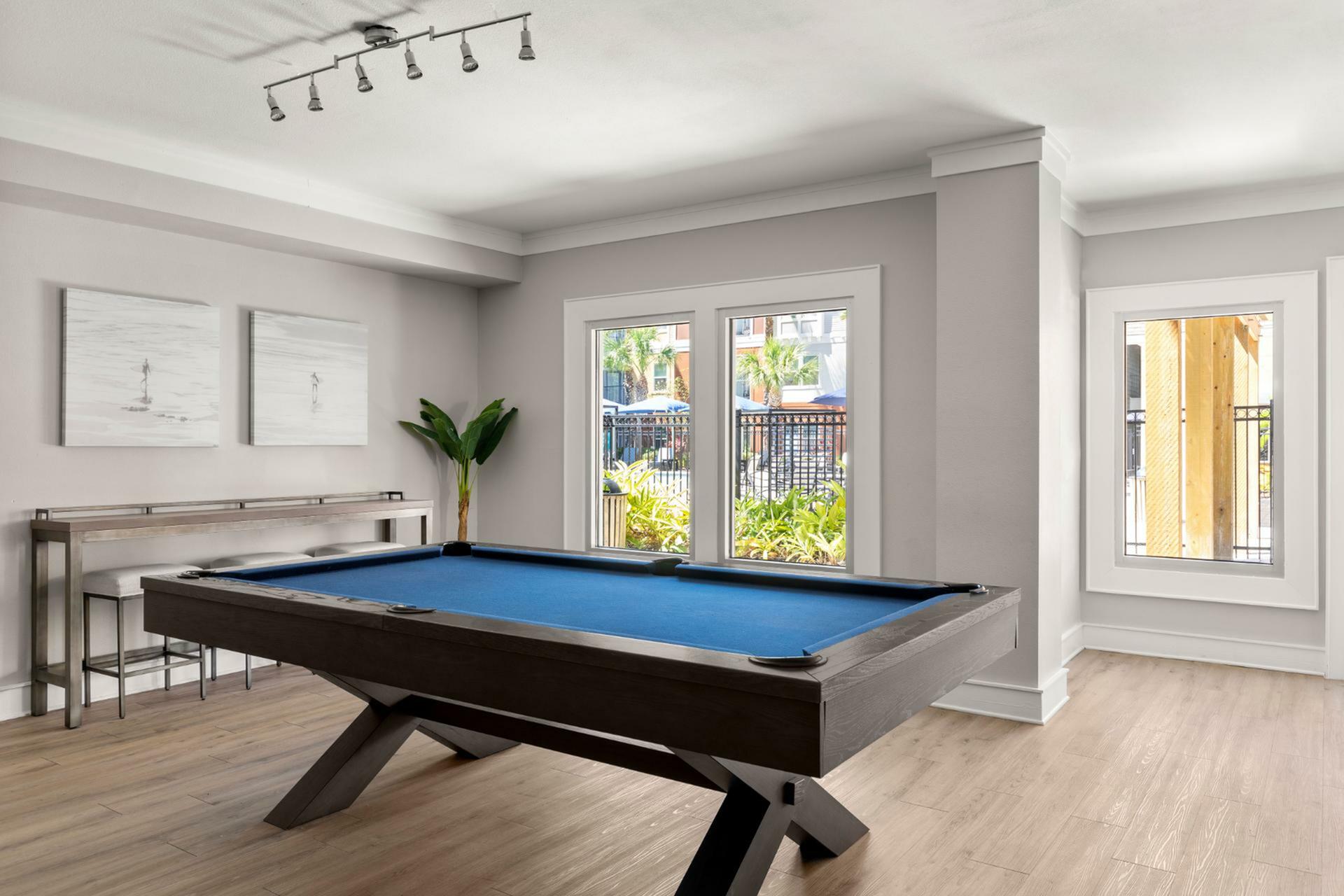 Elegant recreation room with a stylish pool table, modern decor, and bright natural light from large windows.