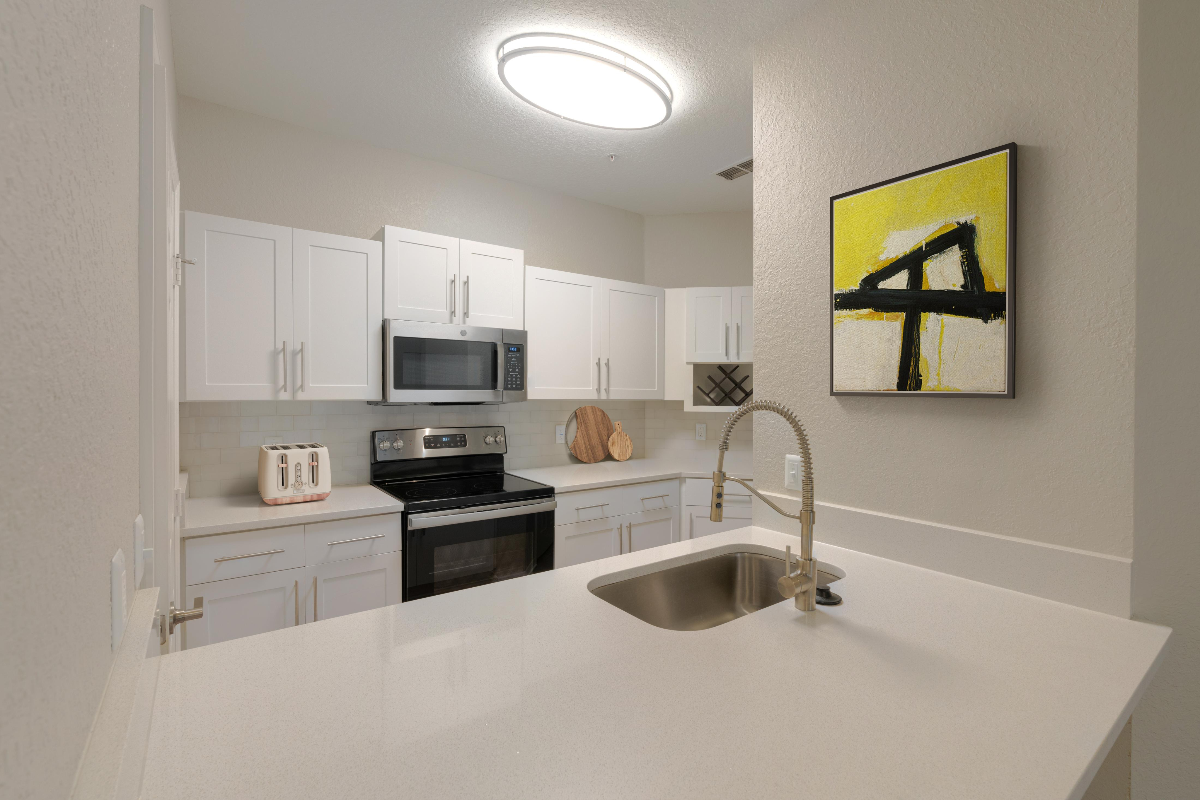 Modern kitchen with sleek white cabinetry, stainless steel appliances, and elegant countertops, enhanced by bright artistic decor.