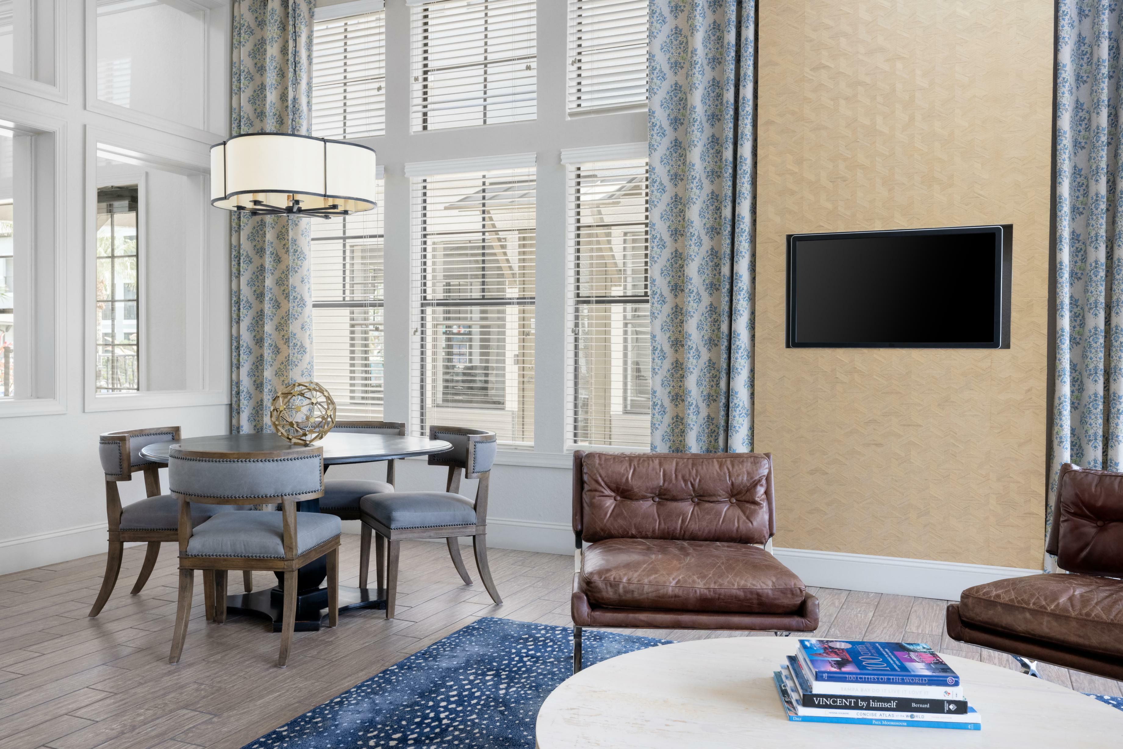 Bright and airy living room with elegant decor, featuring patterned curtains, a stylish round dining table, and comfortable leather seating.