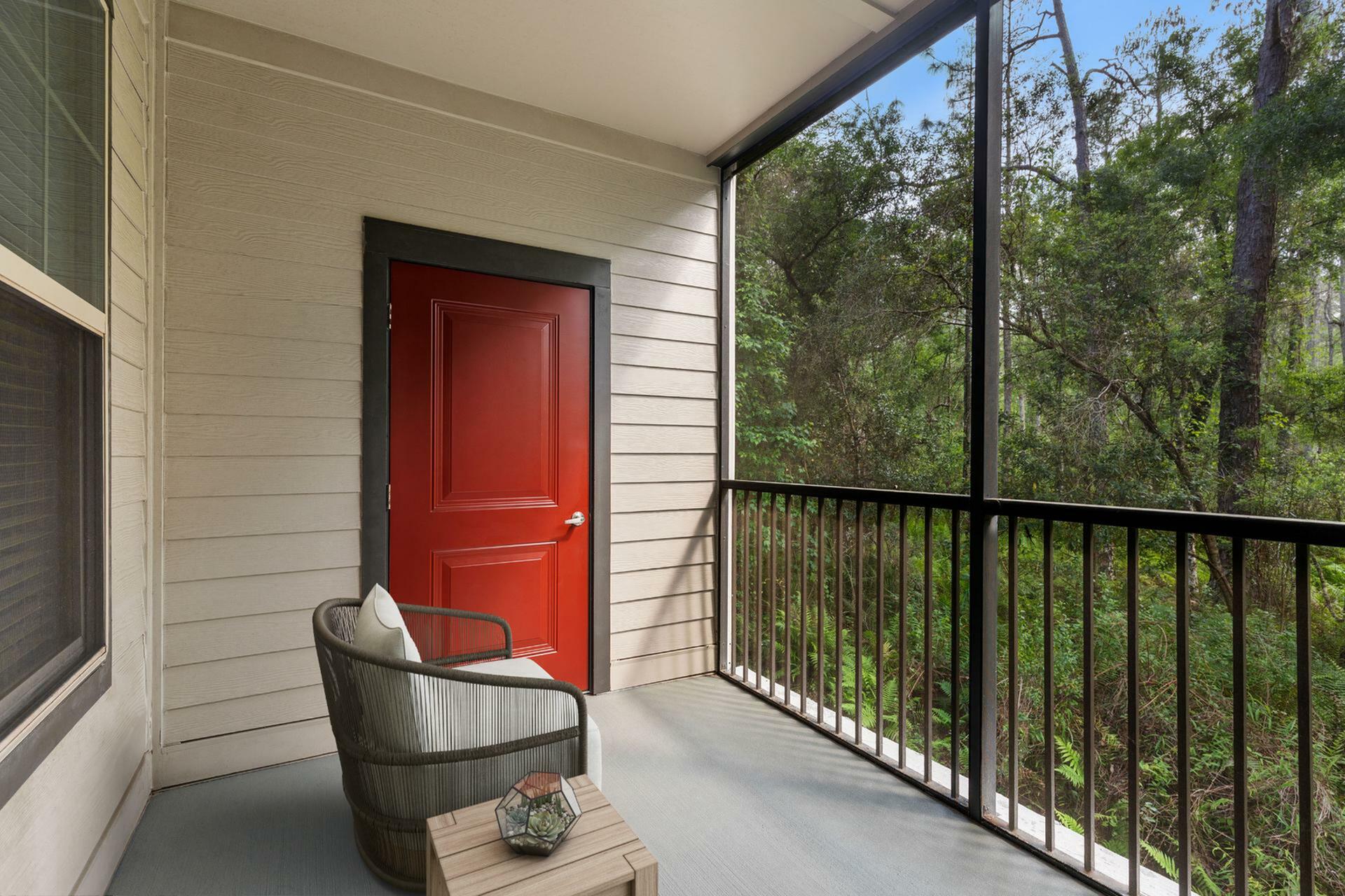 Charming balcony with a vibrant red door, cozy seating, and serene forest views, perfect for relaxation.