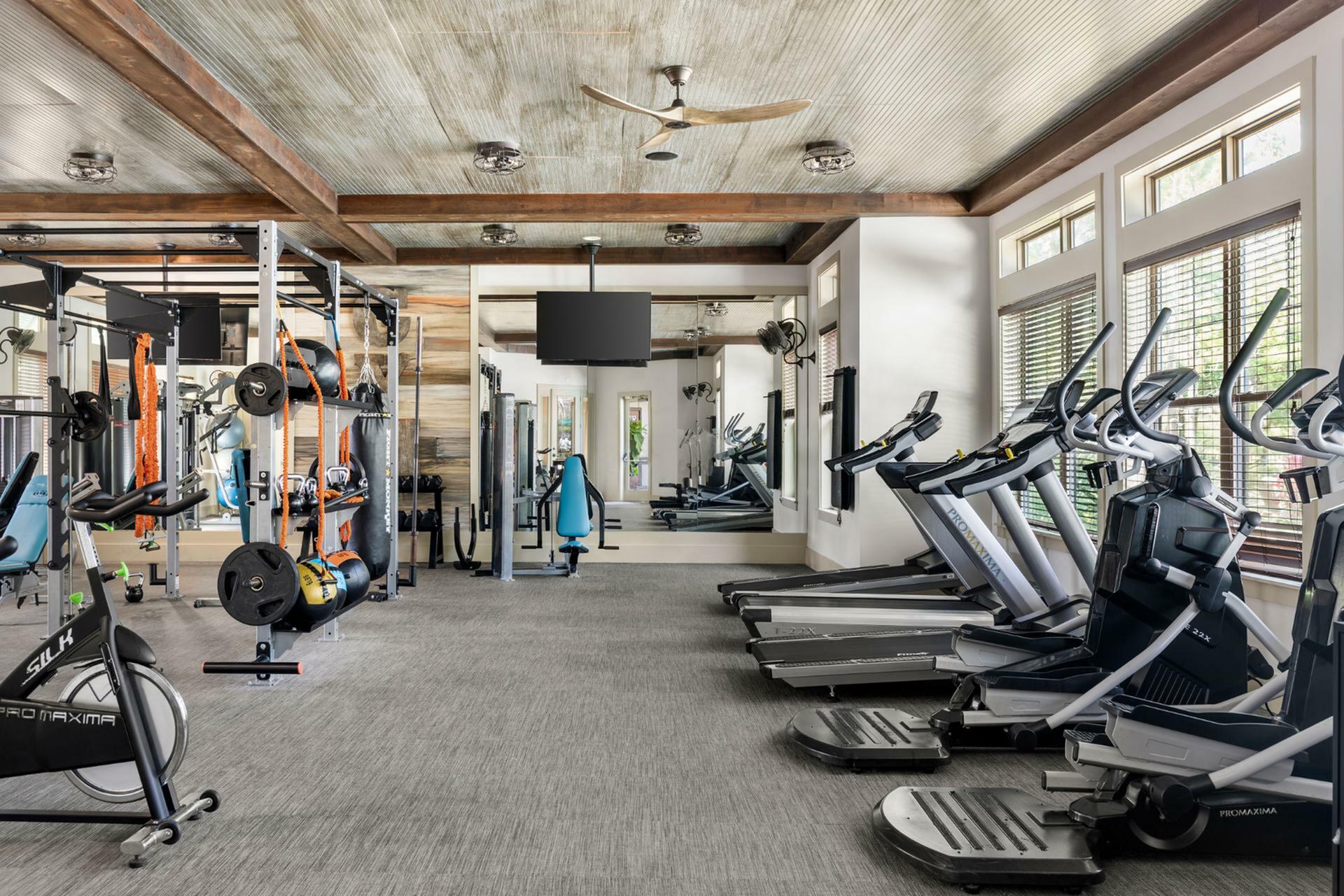 Modern fitness center with state-of-the-art gym equipment, bright windows, and a stylish ceiling fan, offering a vibrant workout environment.