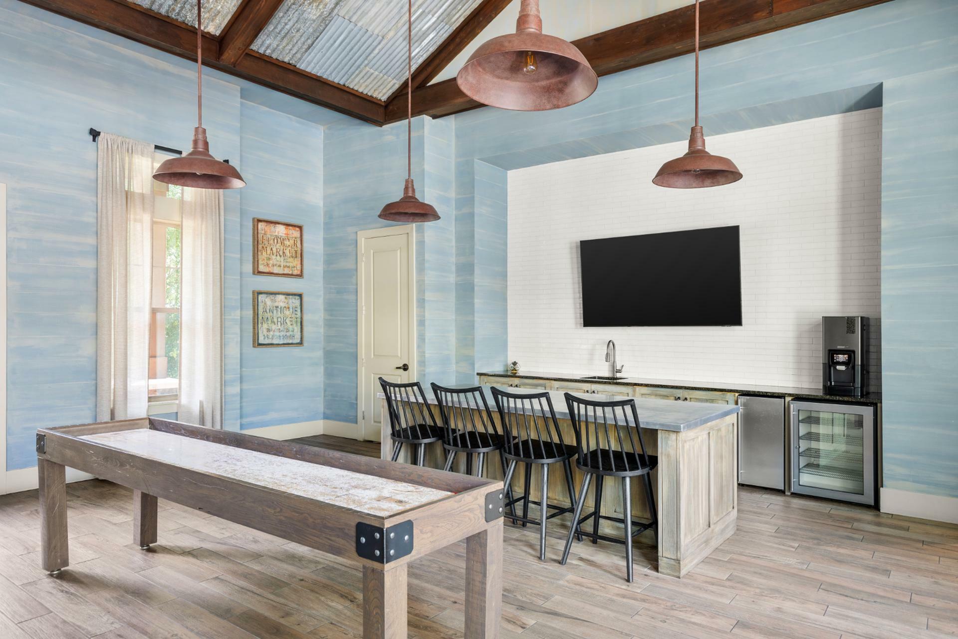 Charming recreational room with a stylish wooden shuffleboard table, modern kitchenette, and cozy seating, topped by rustic pendant lights.