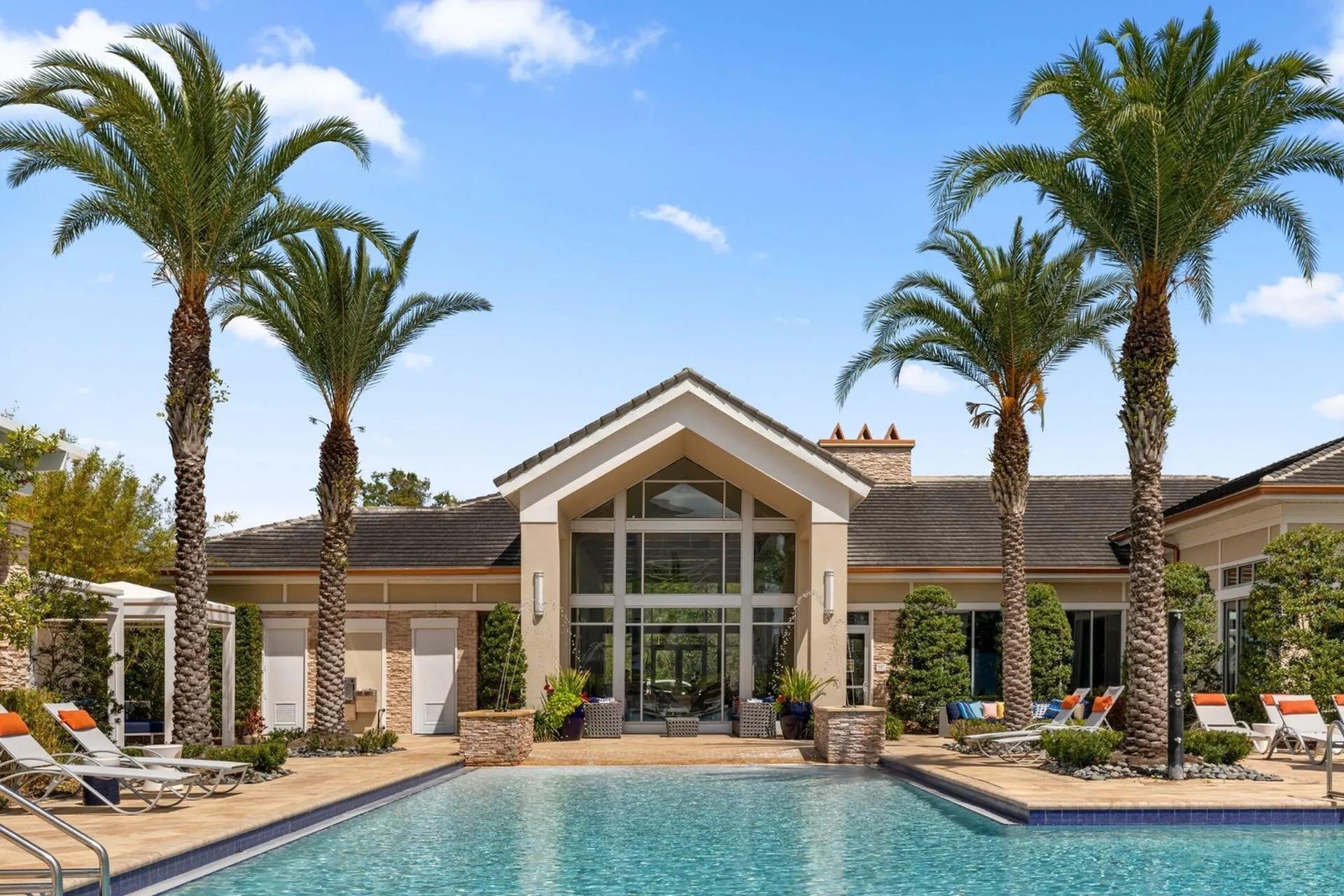 Luxurious apartment complex featuring a stunning outdoor pool with elegant lounge chairs, surrounded by palm trees and modern architecture under a clear evening sky.