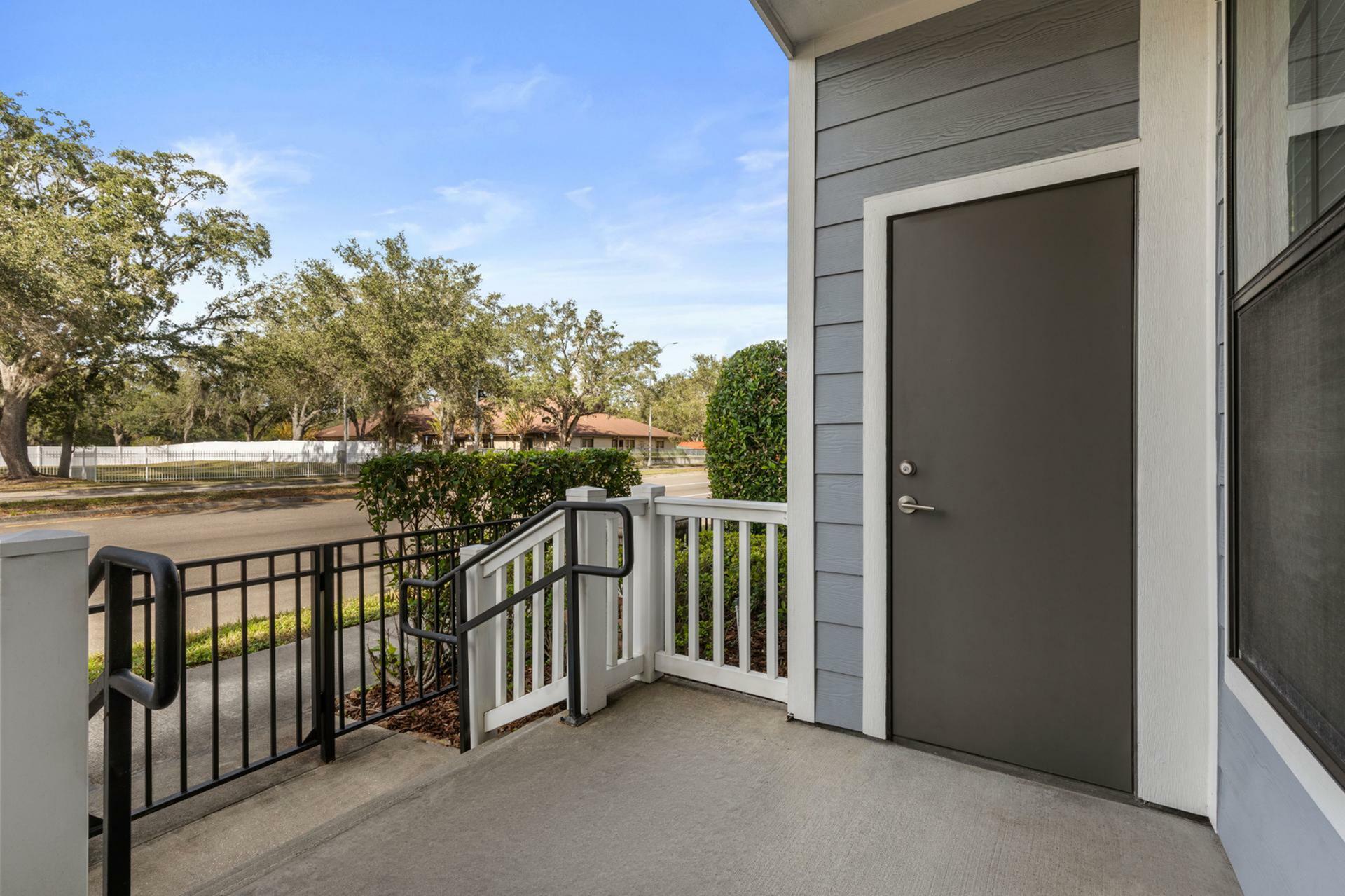 Inviting entryway with modern grey door, charming porch, and lush greenery offering a warm welcome.