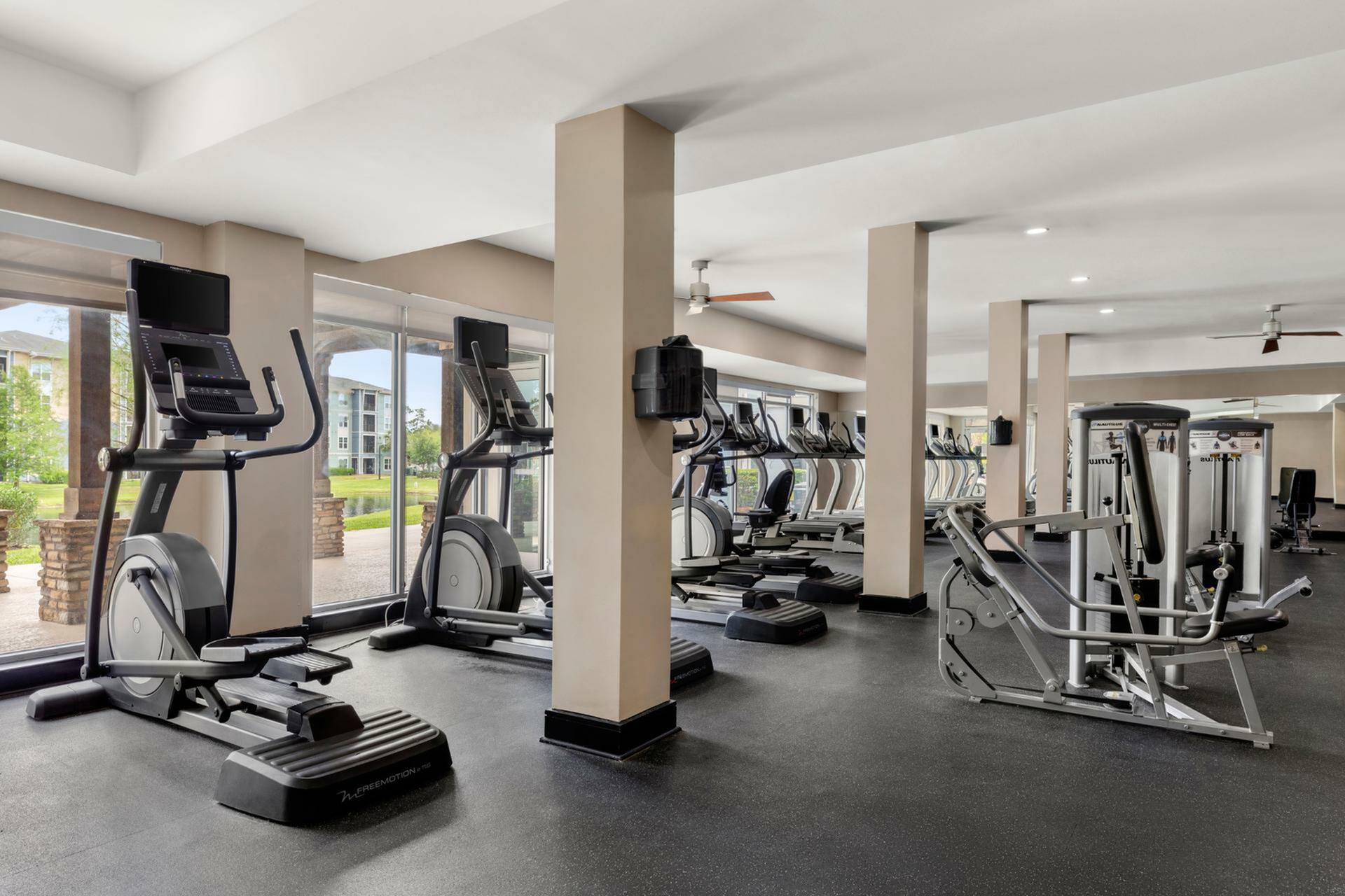 Modern apartment gym featuring state-of-the-art cardio equipment, strength machines, and scenic window views.