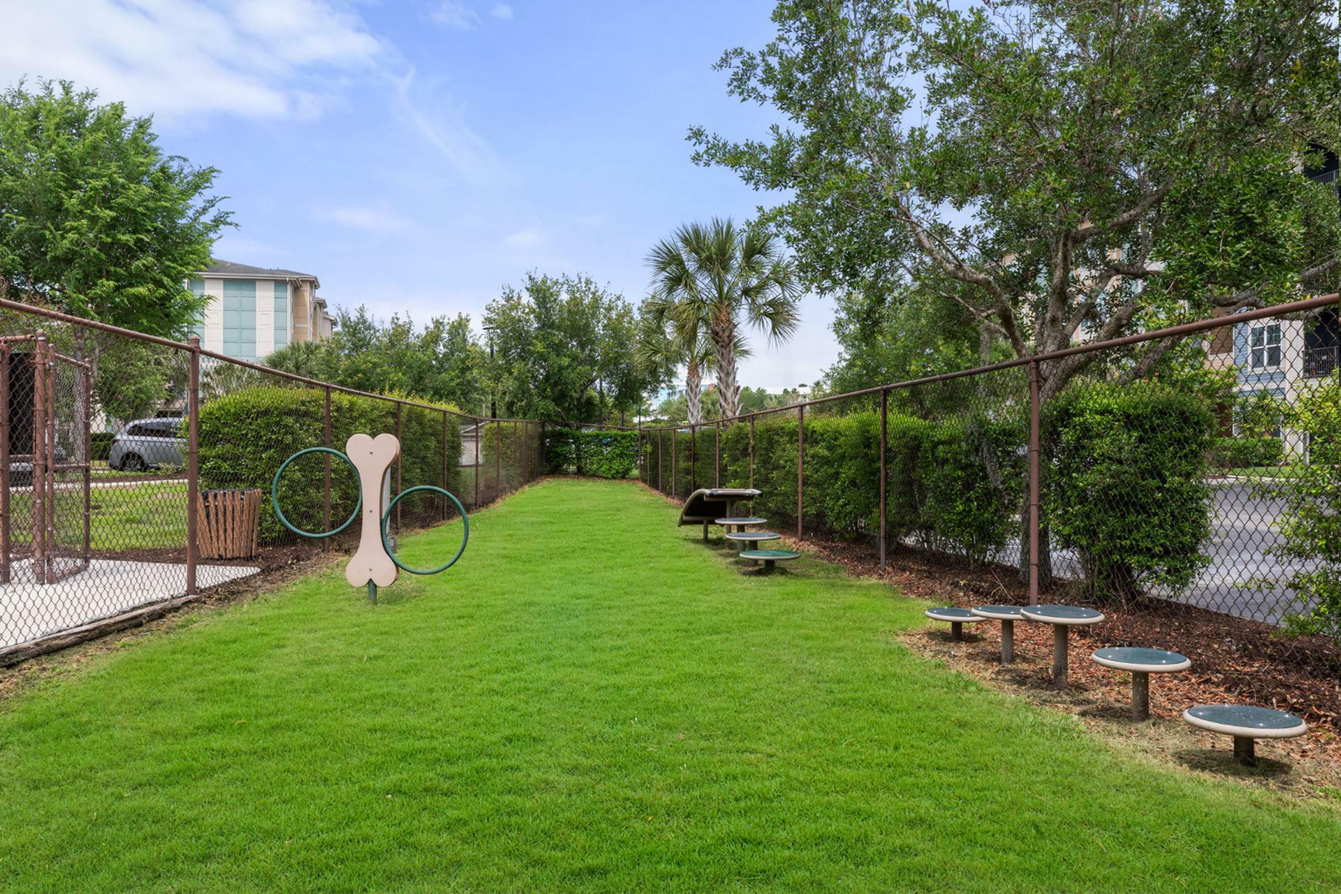 Vibrant apartment dog park with agility course featuring lush green grass and playful equipment, surrounded by secure fencing.