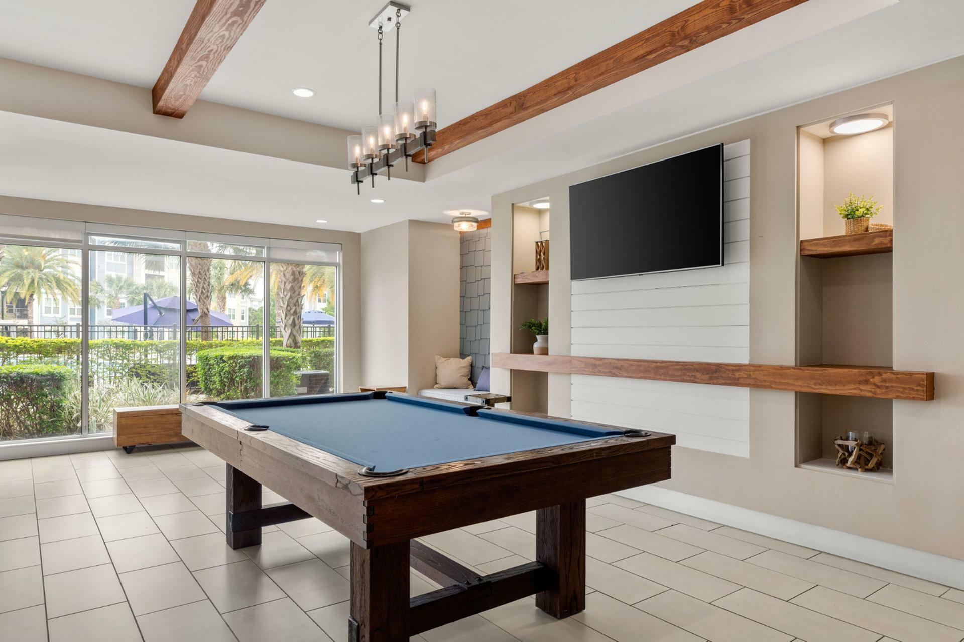 Chic lounge area featuring a sleek pool table, large TV, and stylish decor with a pool view through expansive windows.