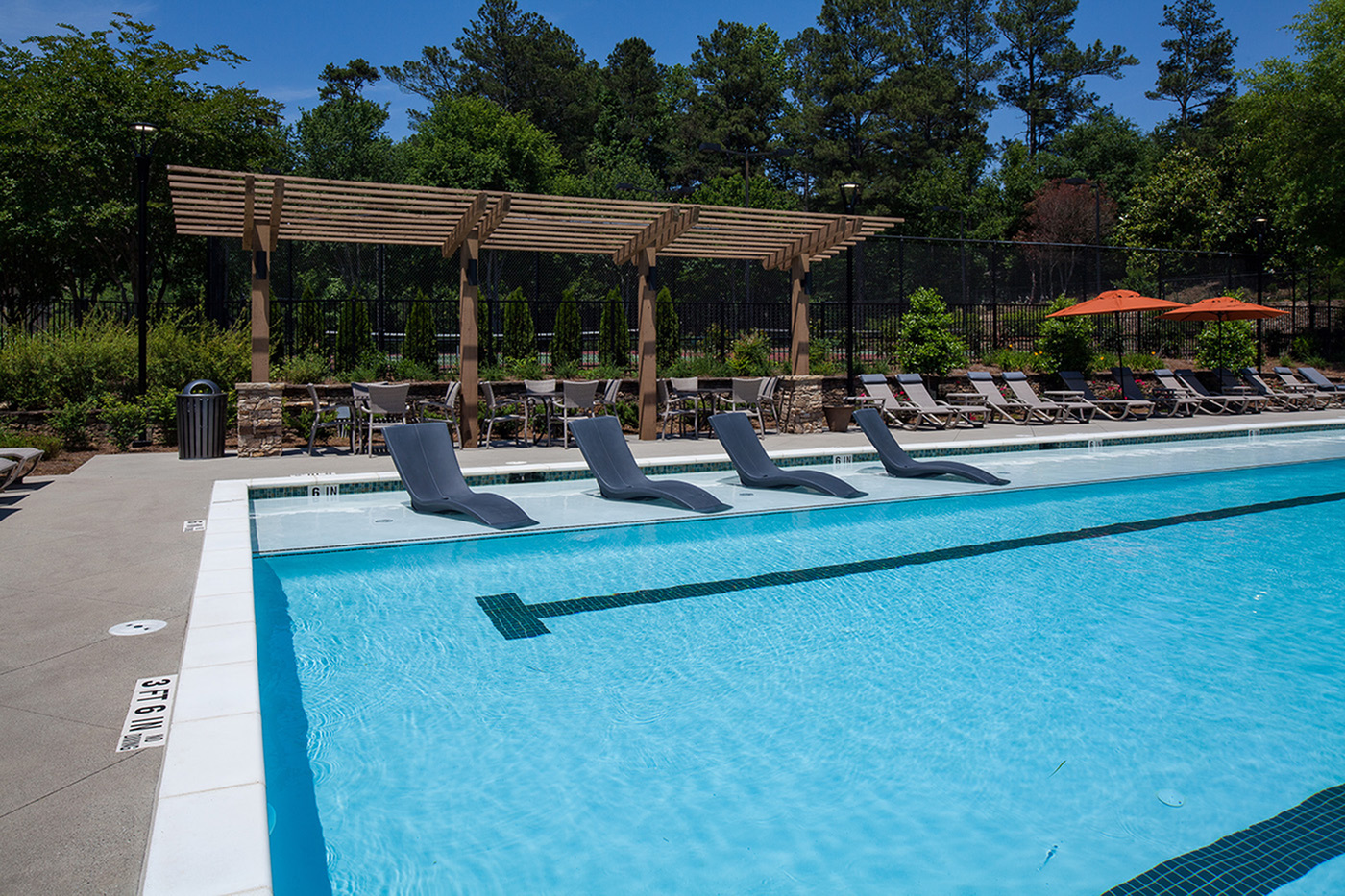 Luxurious outdoor pool area with stylish lounge chairs, shaded pergola, and vibrant greenery, perfect for relaxation and leisure.