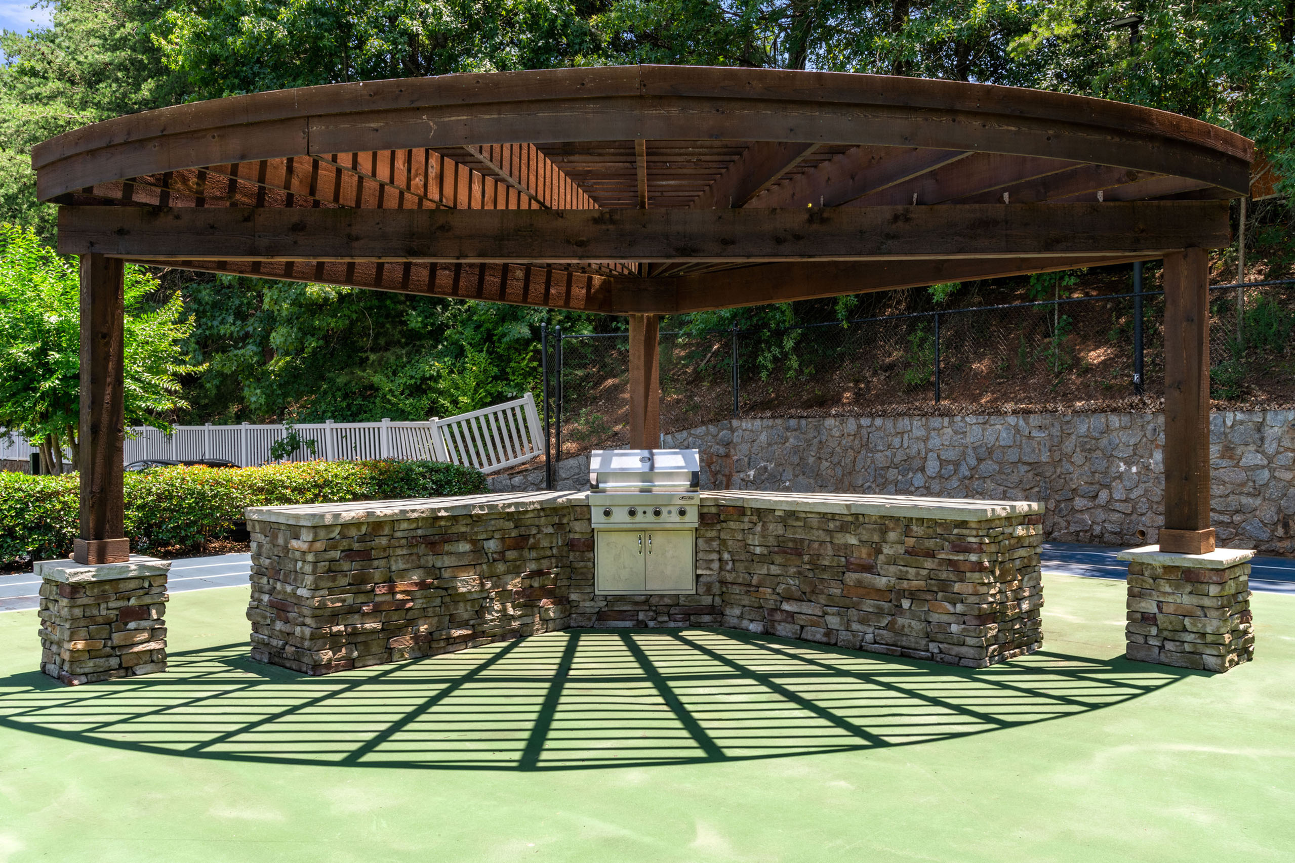 Inviting outdoor kitchen area with a rustic stone grill under a charming wooden pergola surrounded by lush greenery.