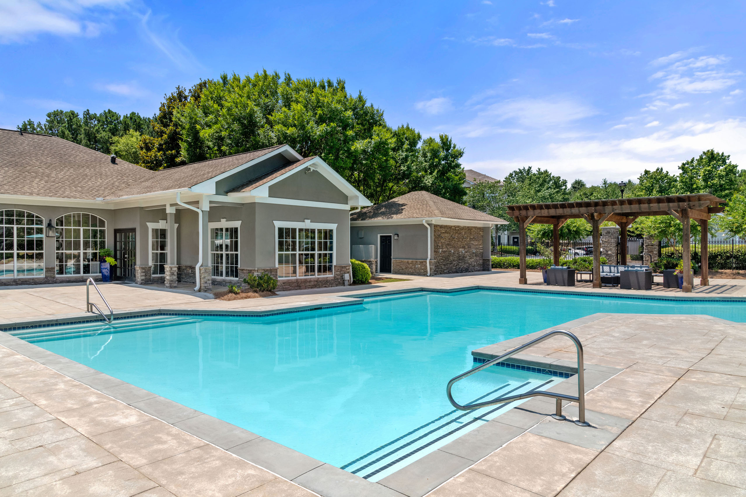 Luxurious apartment pool area with pristine blue waters, elegant pergola, and stylish clubhouse under a clear blue sky.