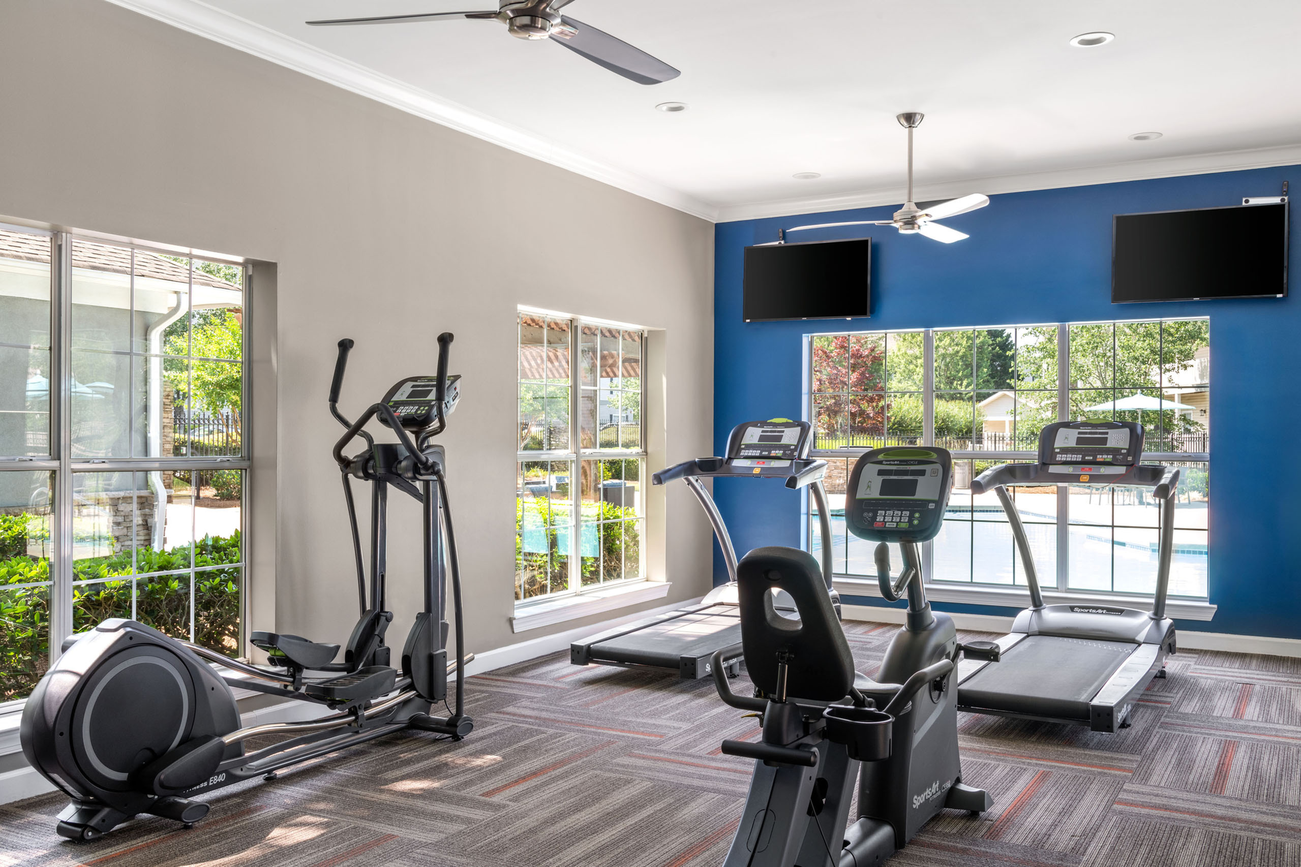 Modern fitness center with natural light, featuring treadmills, ellipticals, and exercise bikes overlooking a serene pool area.