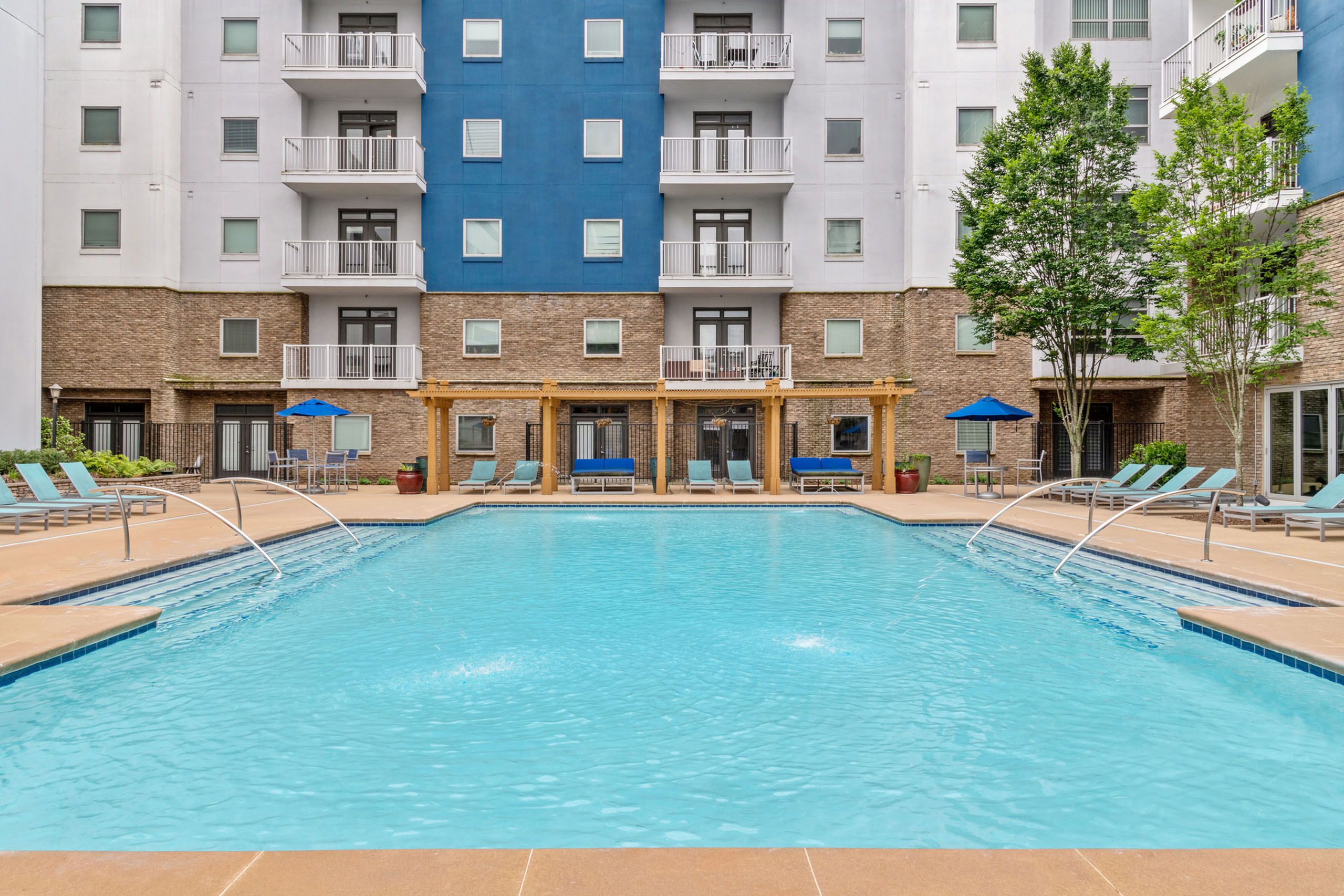 Elegant apartment complex with a sparkling outdoor pool, surrounded by modern balconies and lush greenery, perfect for relaxation and luxury living.