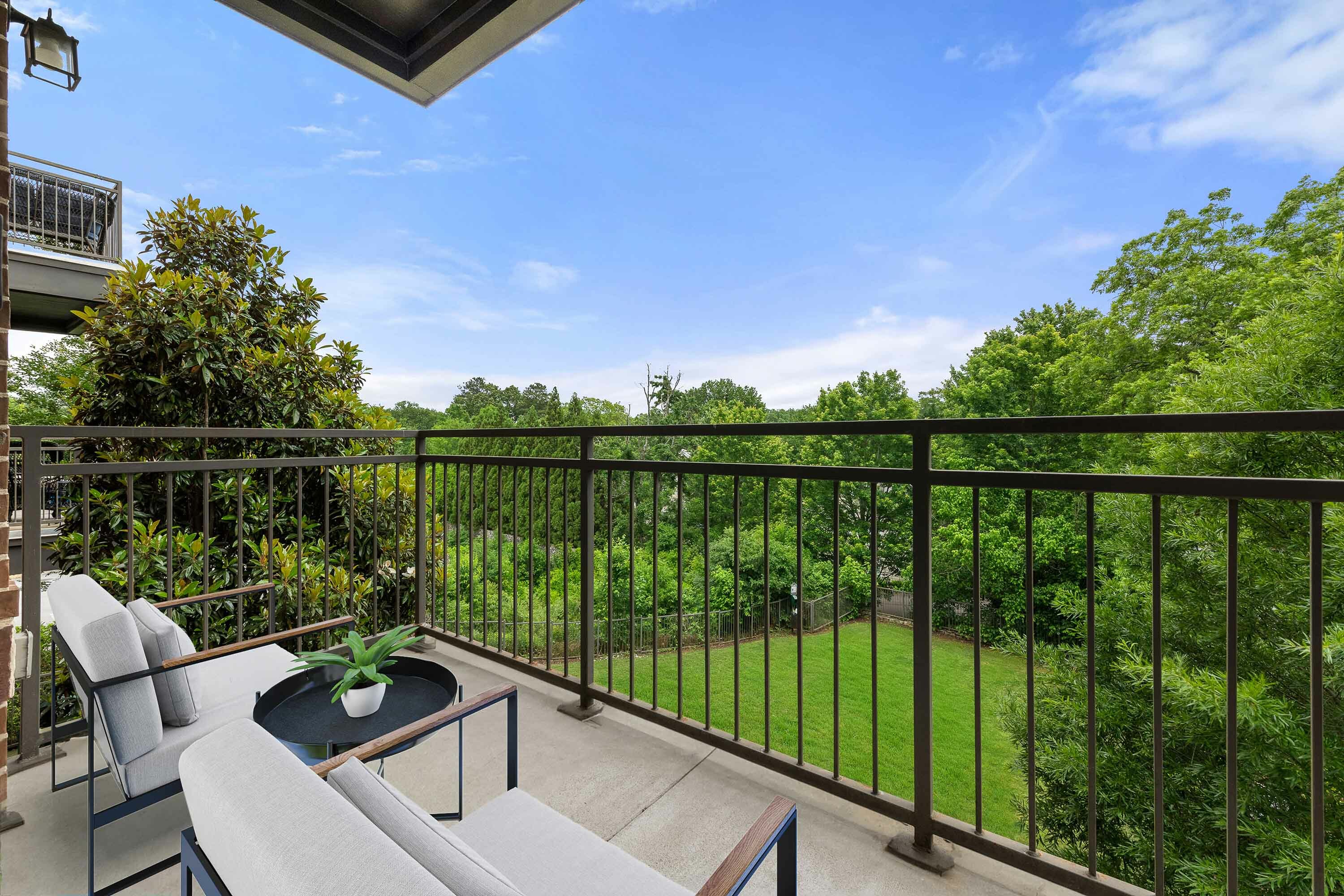 Charming balcony view showcasing lush greenery and blue skies, perfect for relaxing in comfortable modern seating.