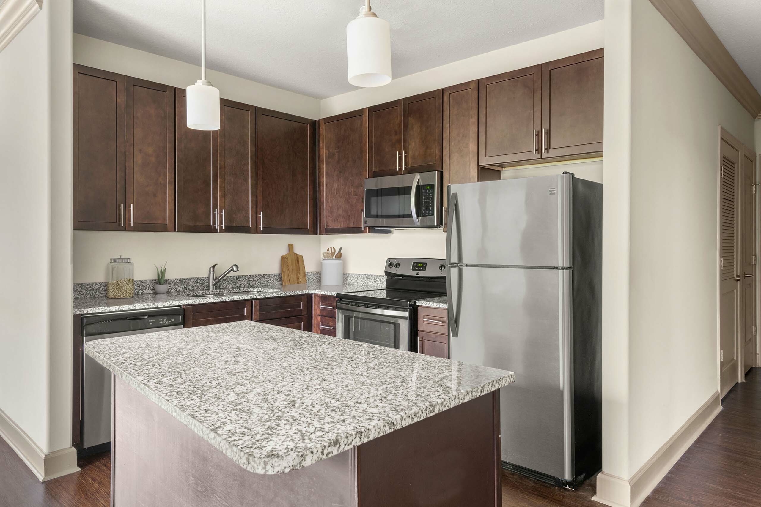 Elegant kitchen with dark wood cabinets, granite countertops, and stainless steel appliances, featuring a central island under modern pendant lighting.