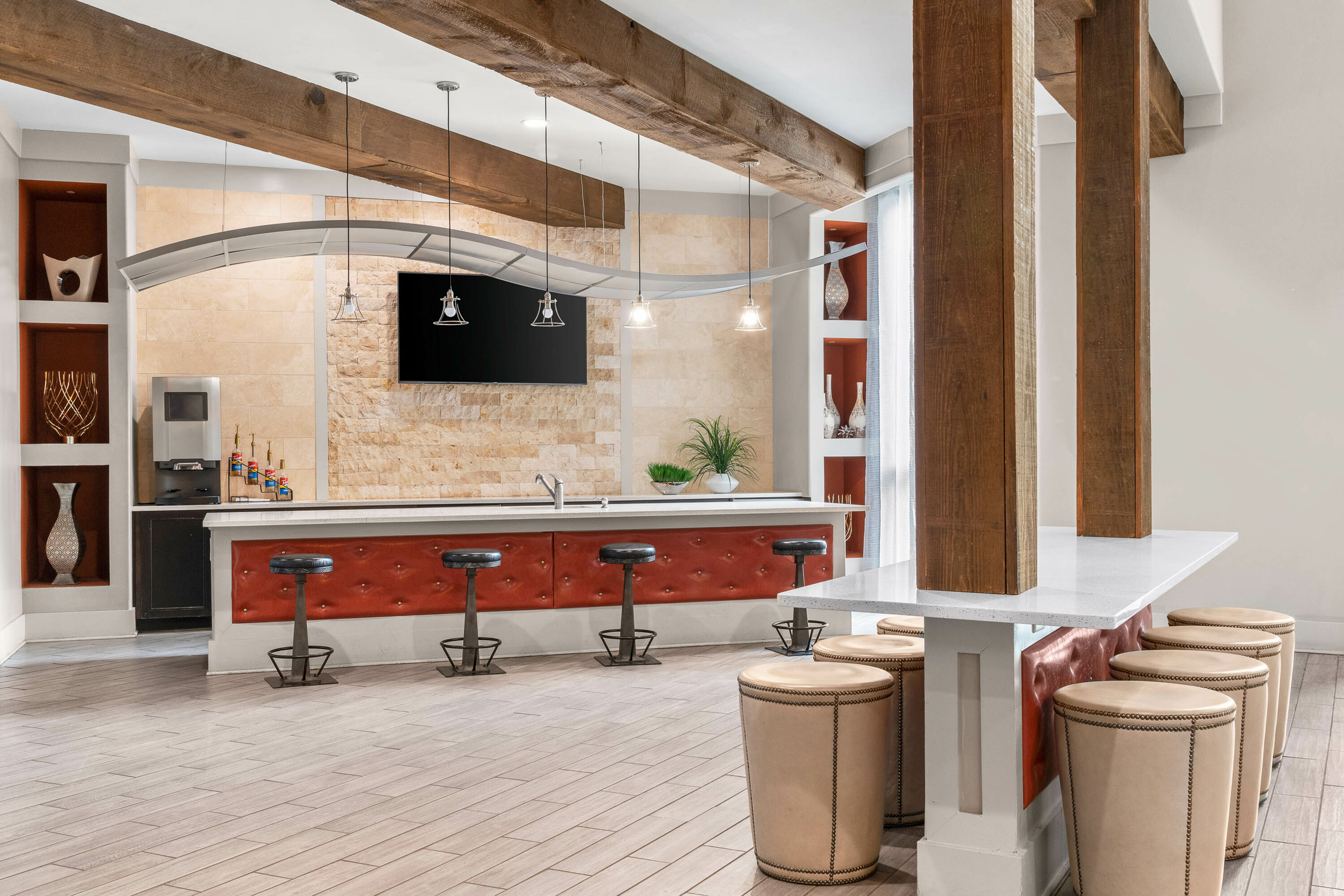 Chic modern kitchen area with plush red seating, industrial bar stools, and sleek decor under rustic wooden beams.