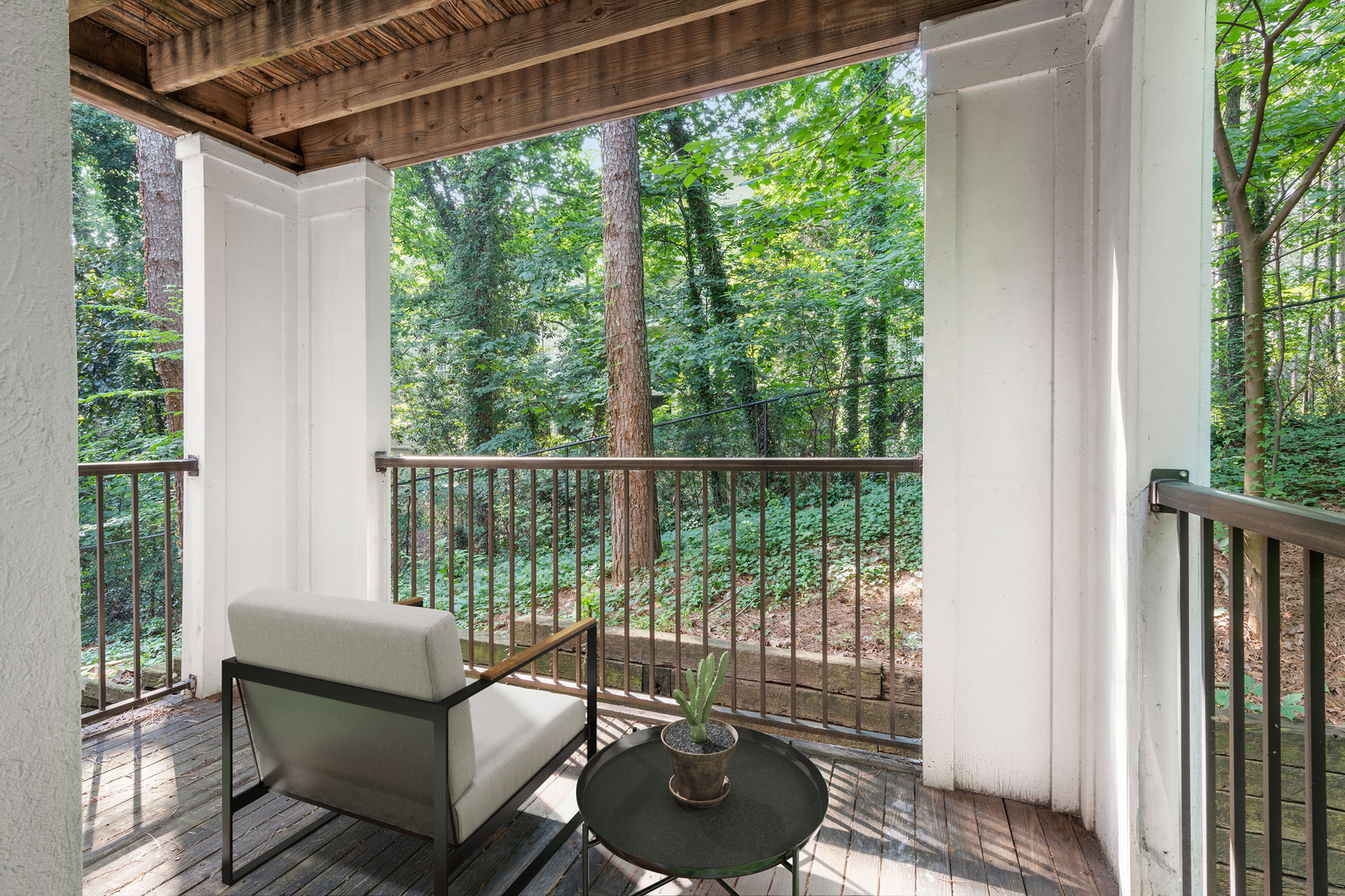 Tranquil apartment balcony with cozy seating, offering serene forest views and modern railing.
