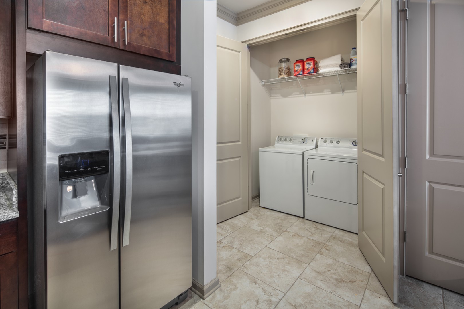 Modern apartment laundry area with sleek stainless steel refrigerator, adjacent washer and dryer, and ample storage space.
