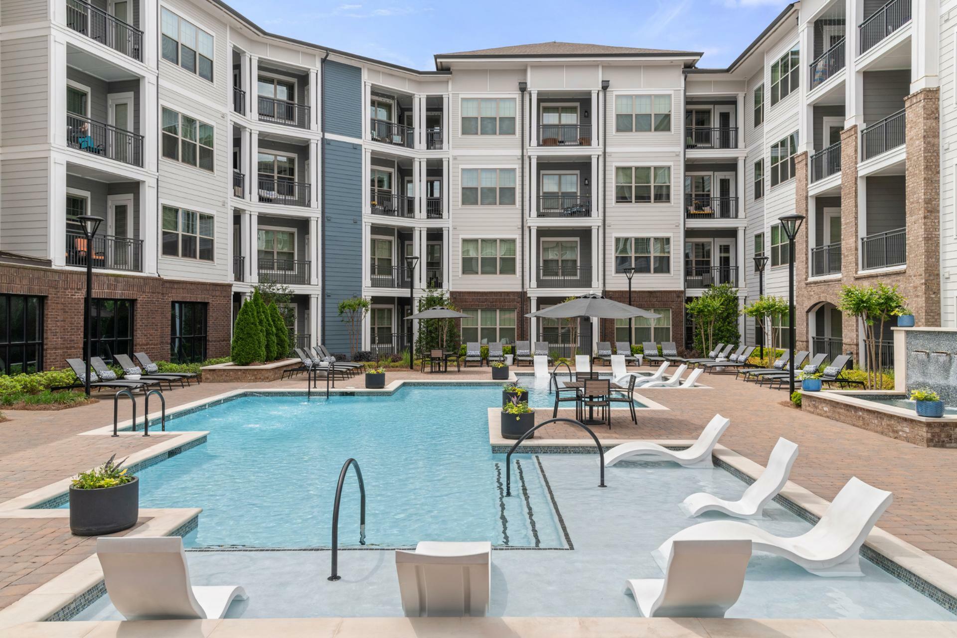 Modern luxury apartment complex with a sparkling swimming pool, elegant poolside seating, and sleek architecture offering spacious balconies.