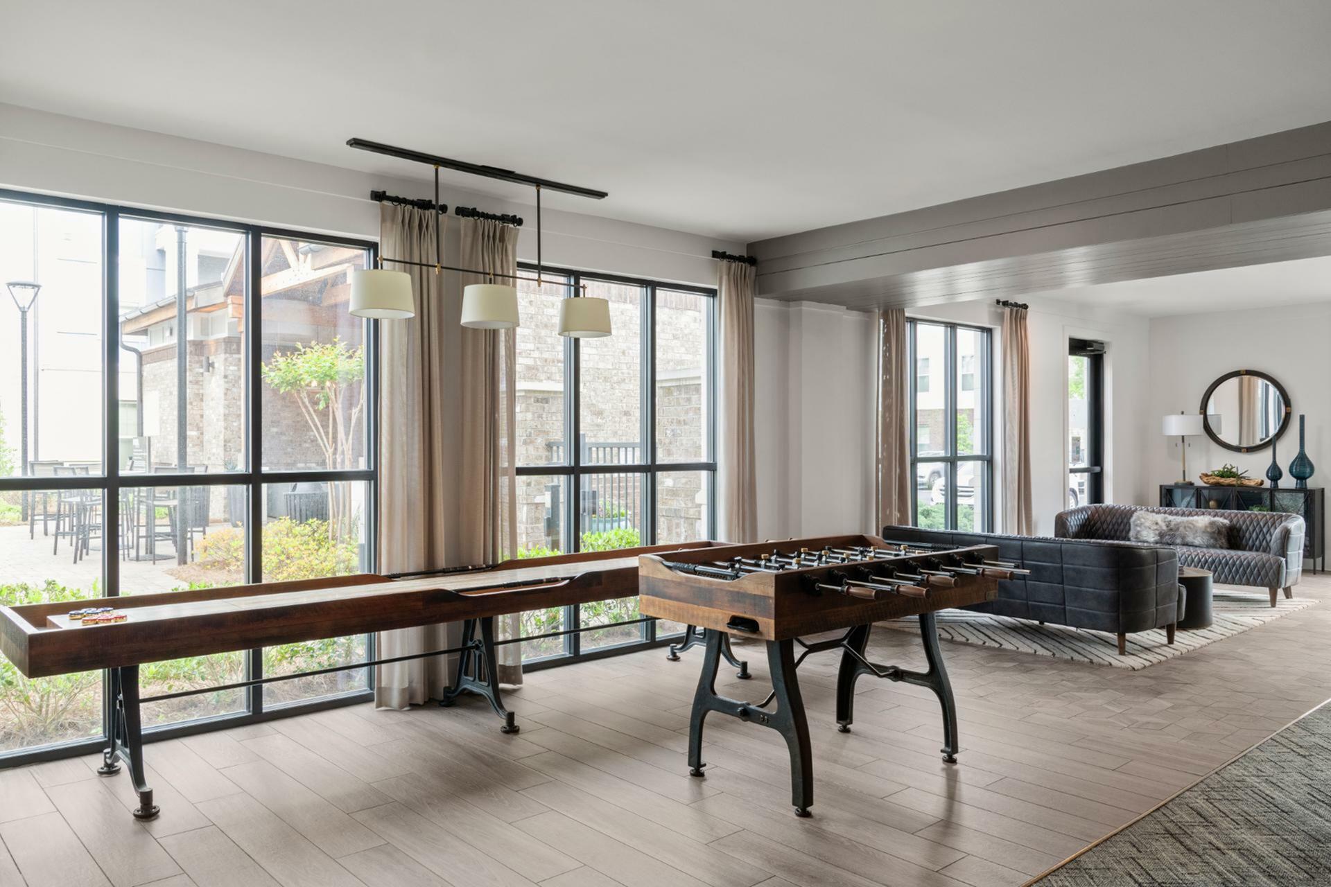 Bright and inviting recreational area featuring foosball and shuffleboard tables, sleek seating, and ample natural light from large windows.
