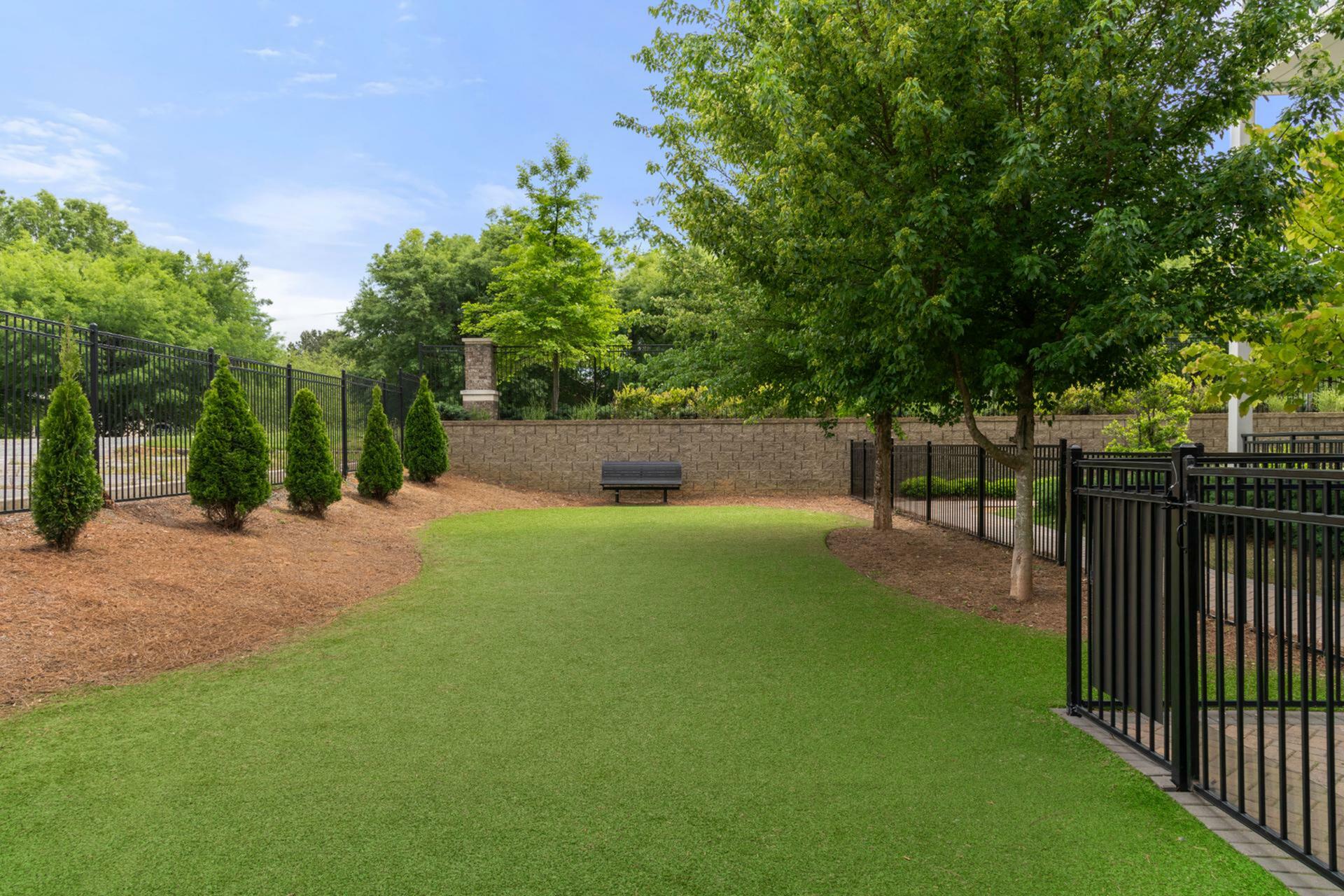Charming green courtyard with lush trees, manicured lawn, and a cozy bench, enclosed by elegant fencing.