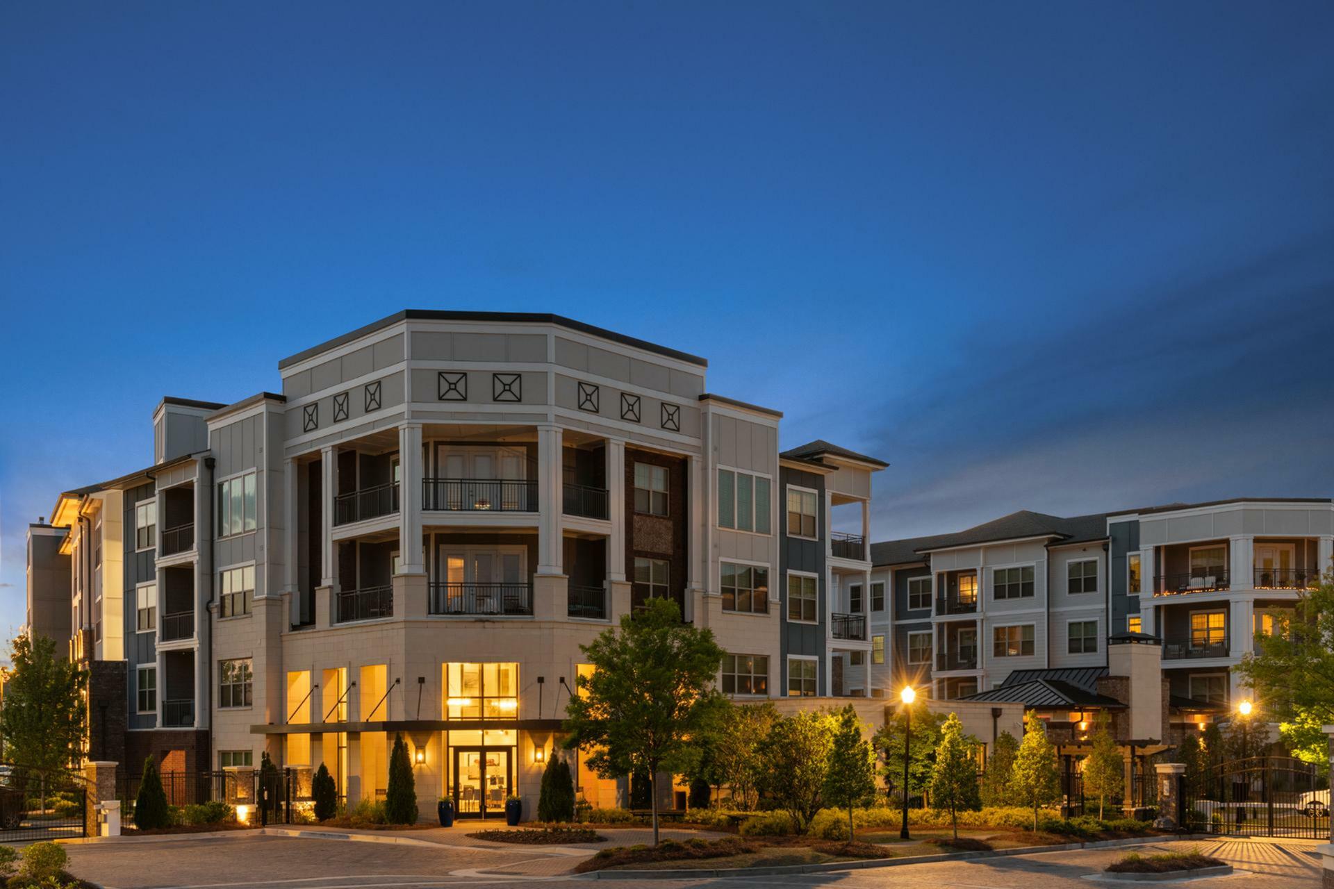 Elegant apartment complex illuminated at dusk, featuring modern architecture and lush landscaping, promising luxurious urban living.
