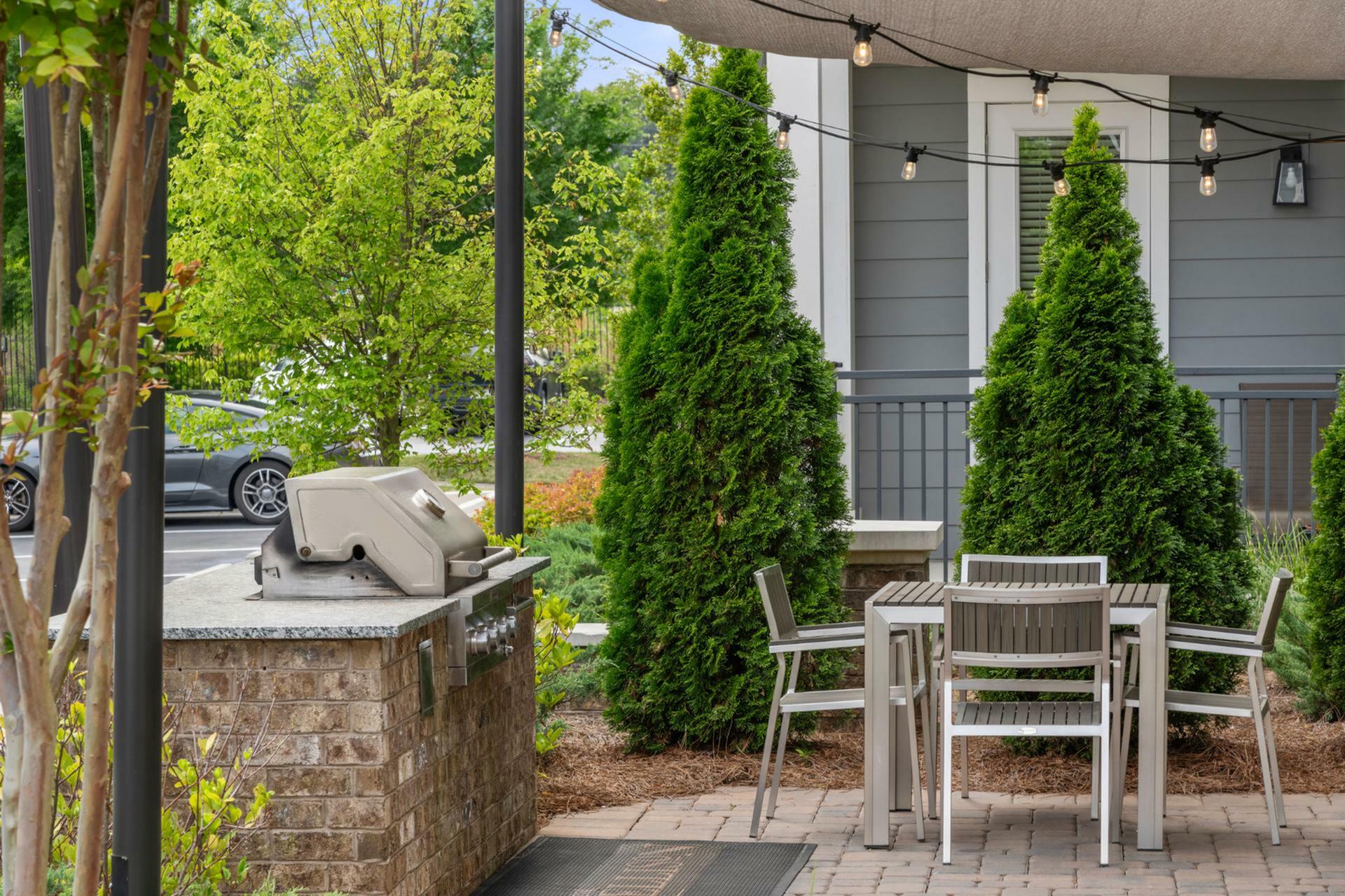 Charming outdoor patio with modern grill, elegant dining set, and lush greenery, perfect for relaxing and entertaining.