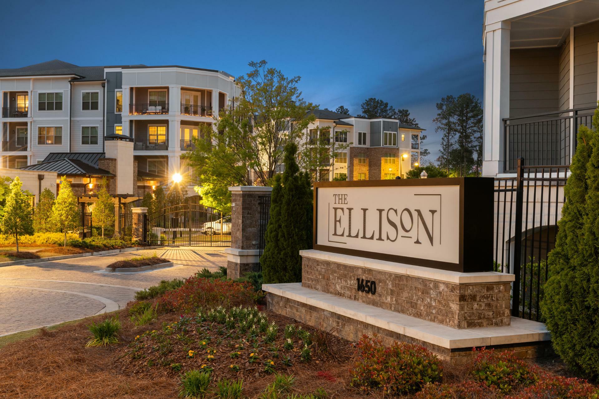 Elegant entrance to The Ellison, showcasing modern architecture and lush landscaping under a twilight sky.