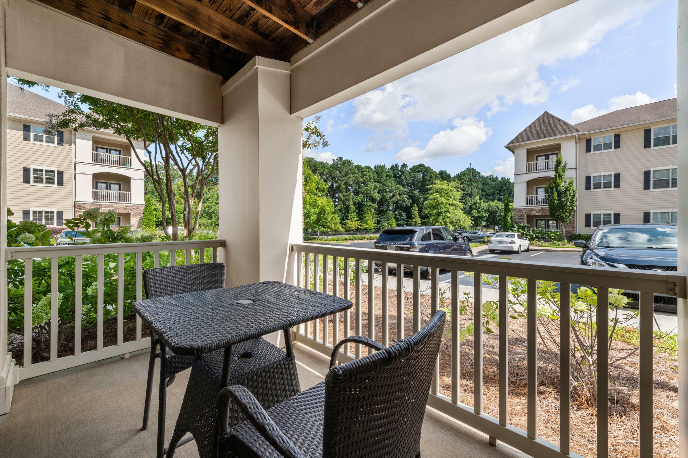 Inviting patio view from an apartment, featuring wicker furniture and overlooking a landscaped courtyard with modern buildings and lush greenery.