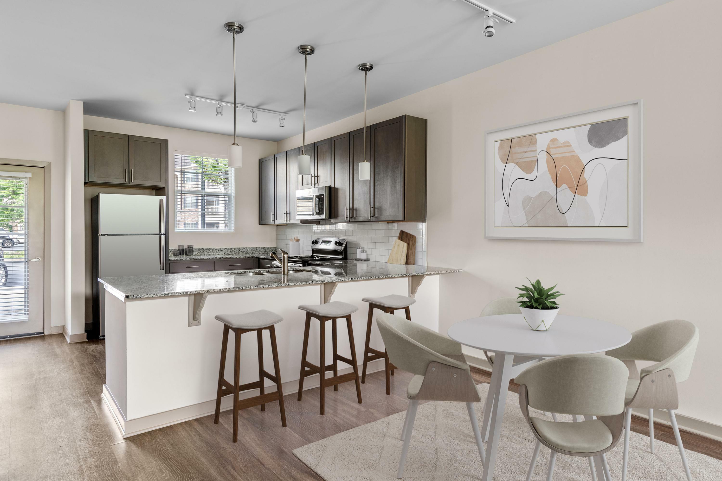 Modern kitchen with sleek granite countertops, stylish bar stools, and contemporary art enhancing a bright dining area.