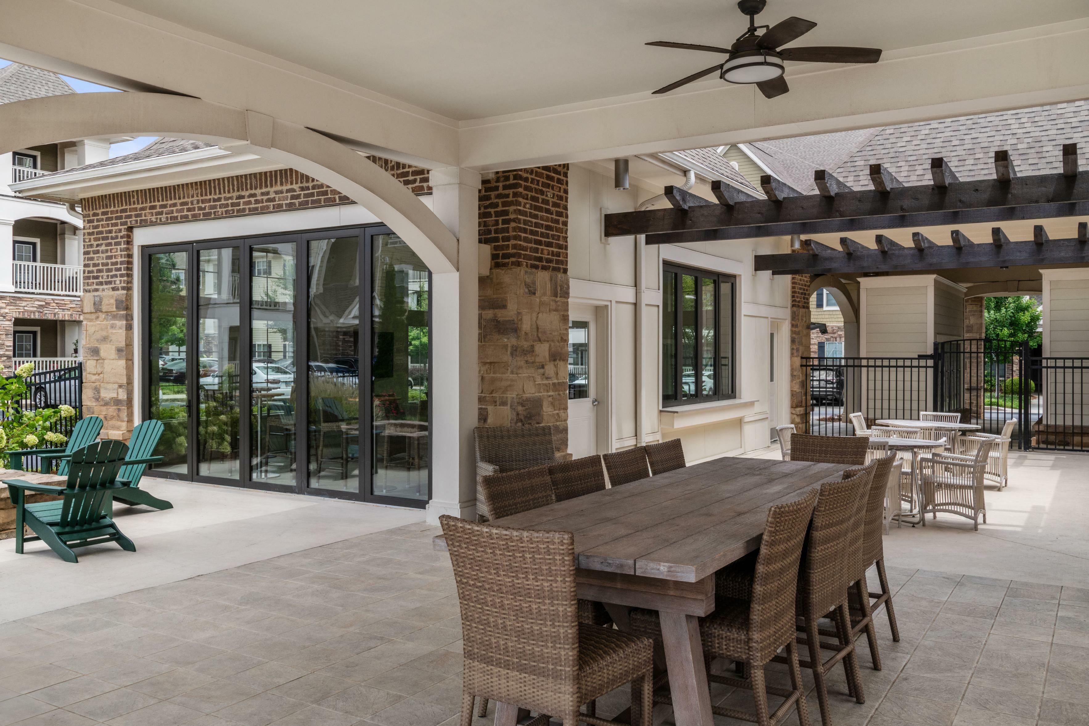 Charming outdoor lounge with rustic wooden dining set, wicker chairs, and lush greenery views, perfect for entertaining.