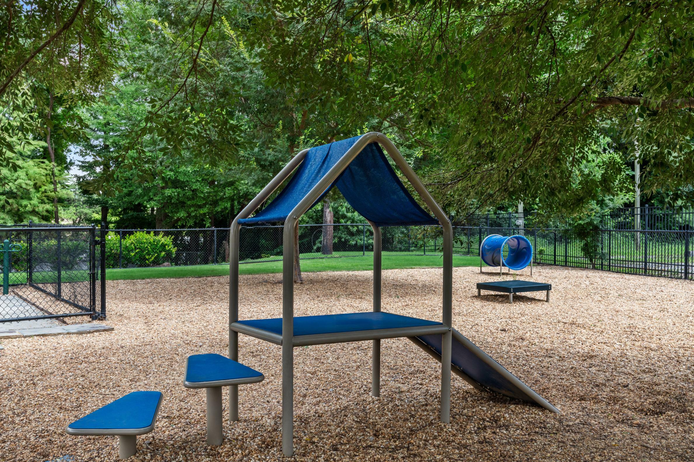 Charming outdoor play area with playground equipment set among lush green trees, perfect for family enjoyment and children\'s activities.