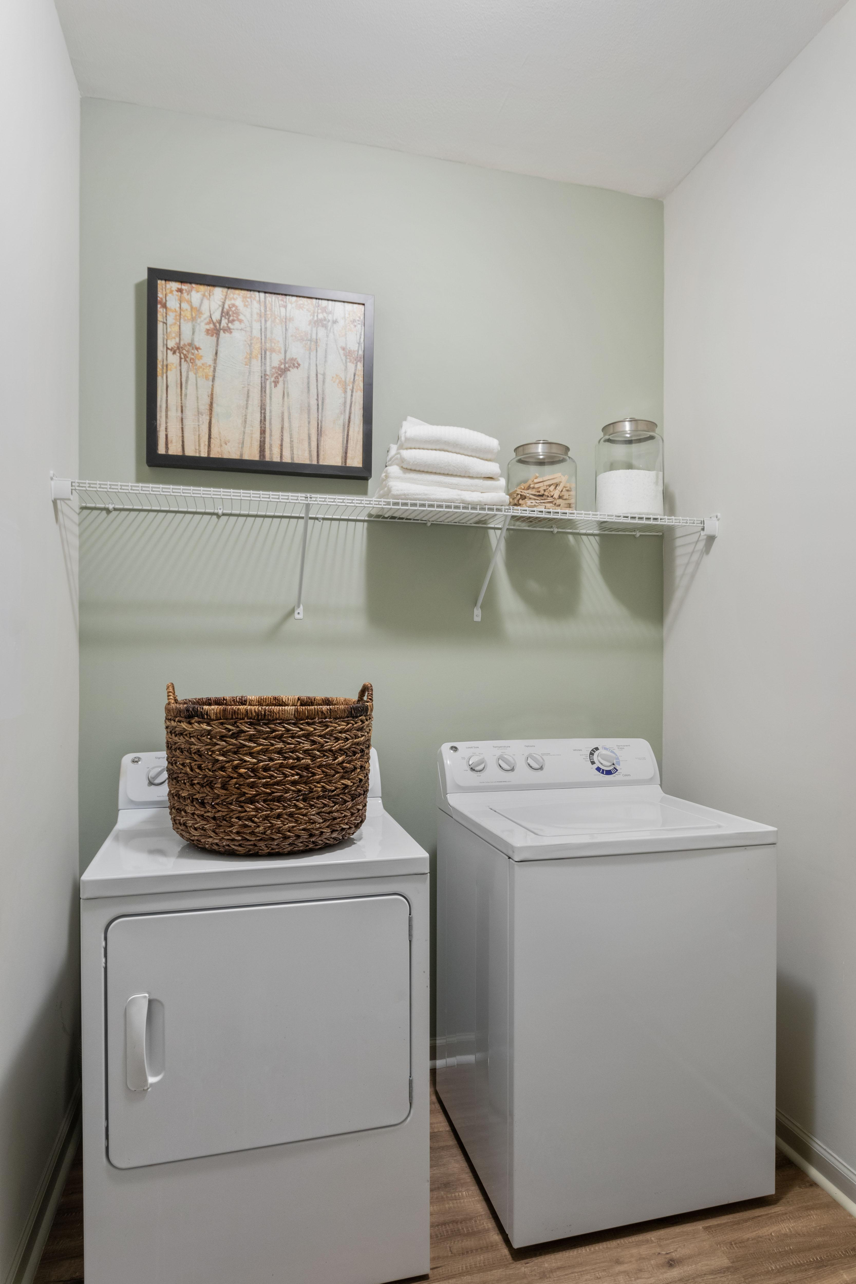 Chic laundry room with modern washer and dryer, wicker basket, and wall art, offering practical elegance for effortless living.