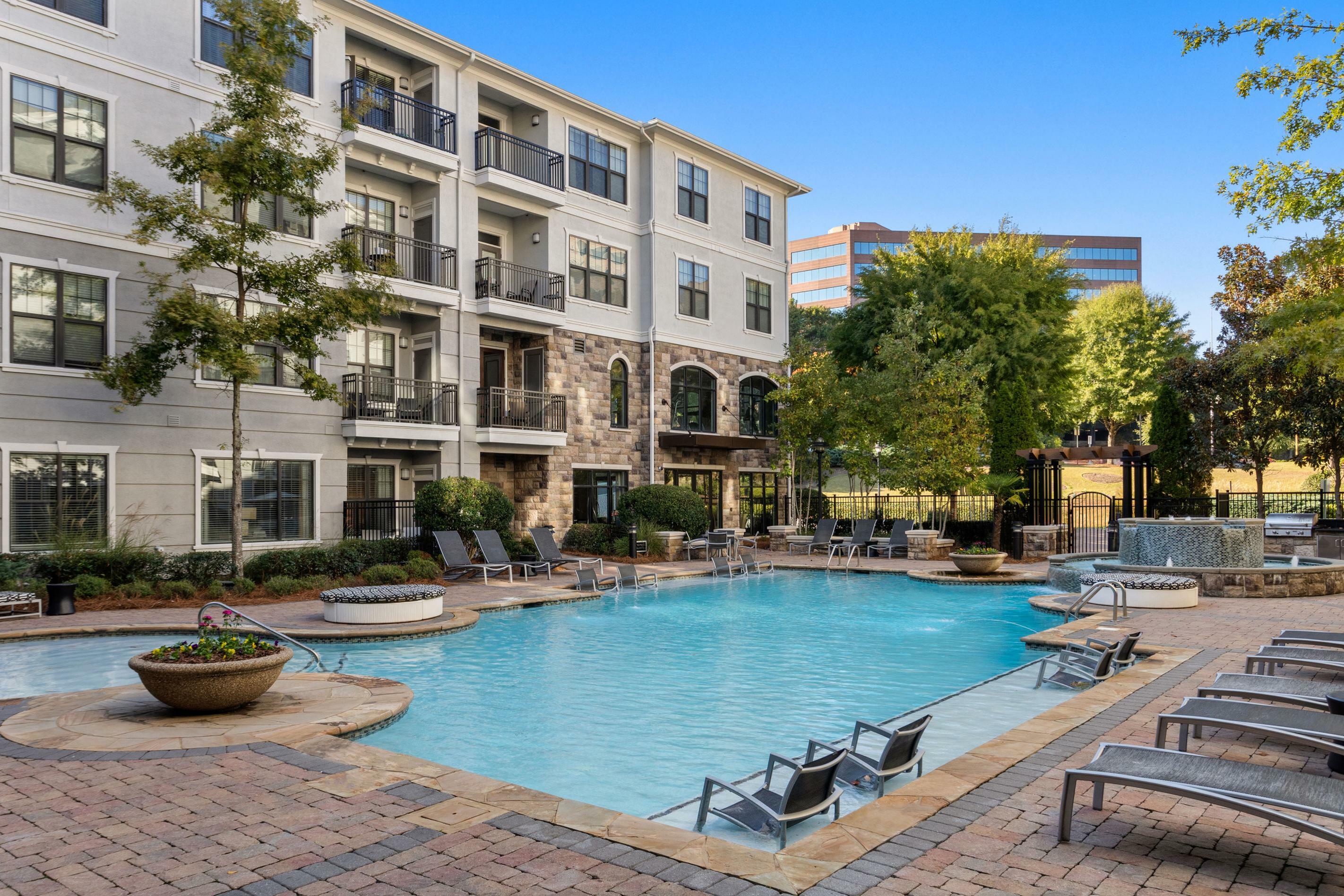 Luxurious apartment building with a sparkling outdoor pool, surrounded by lush greenery and comfortable lounge chairs, perfect for relaxation and entertainment.