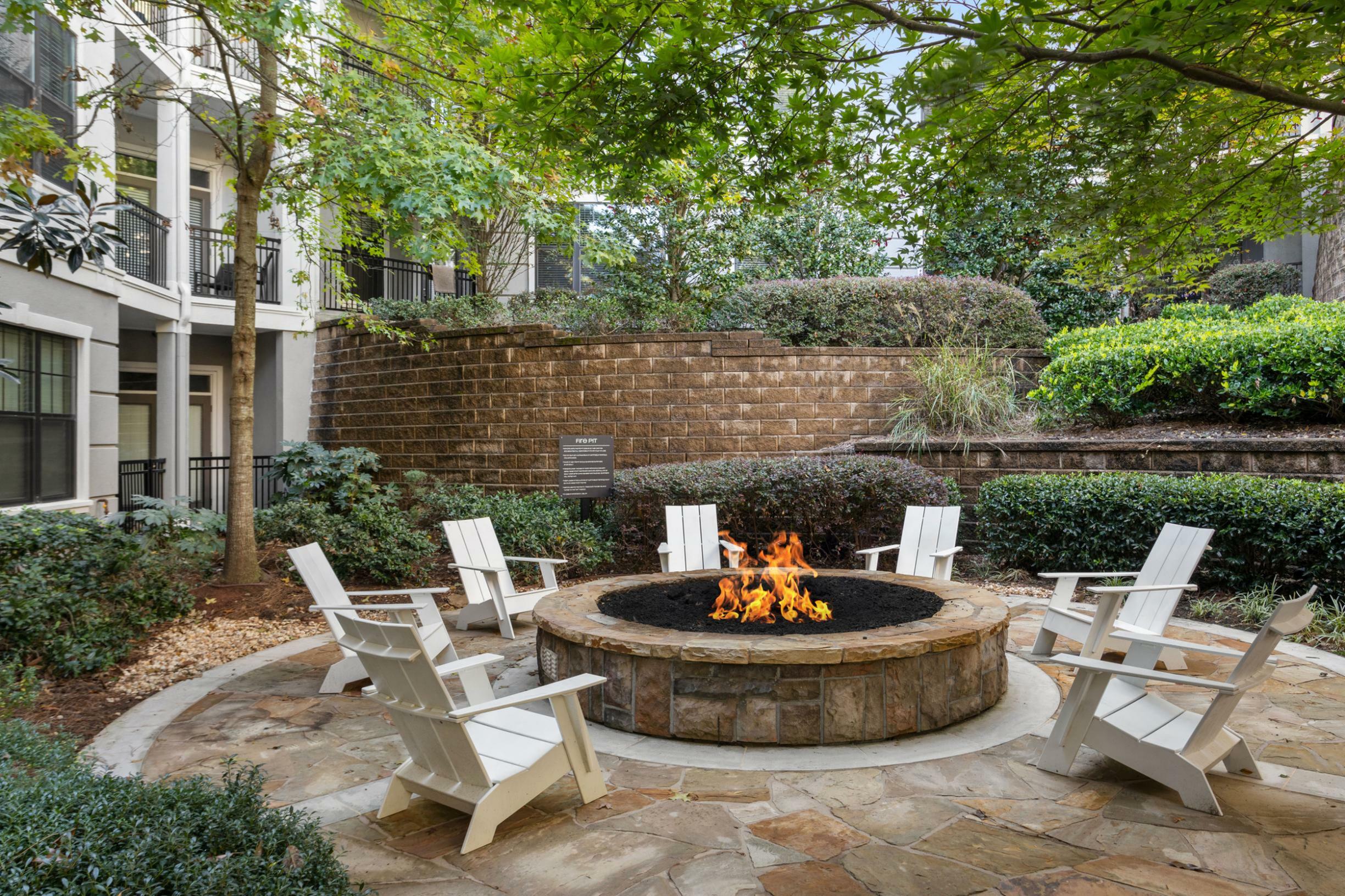 Inviting outdoor patio with a cozy fire pit surrounded by comfortable chairs, enhanced by lush greenery and stylish apartment balconies.