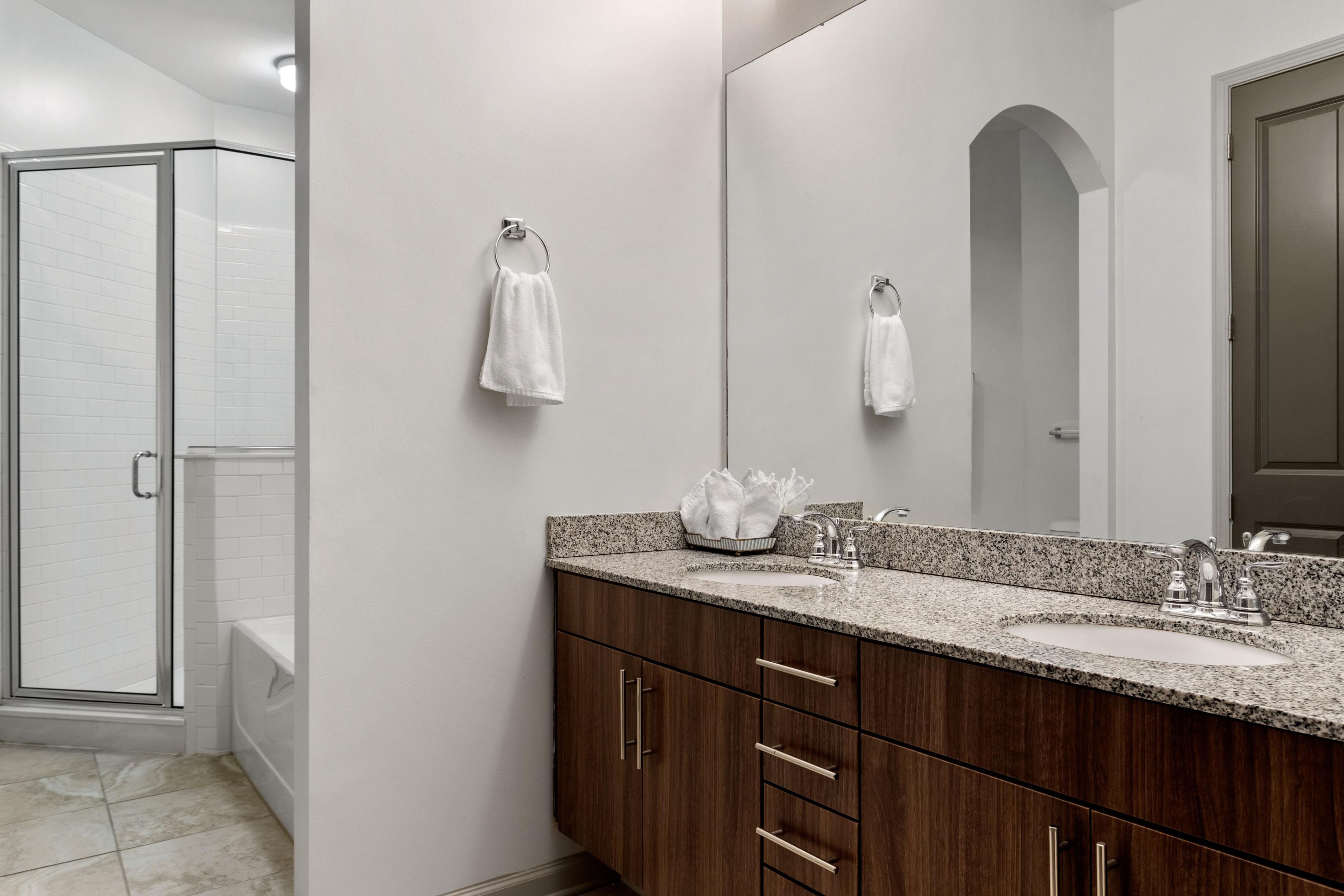 Elegant bathroom with a sleek granite countertop, dual sinks, and a modern glass shower, offering a stylish and functional space.