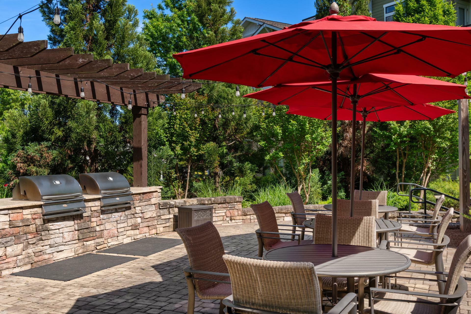 Inviting outdoor patio with stylish seating and vibrant red umbrellas, perfect for entertaining under the pergola with modern grills.