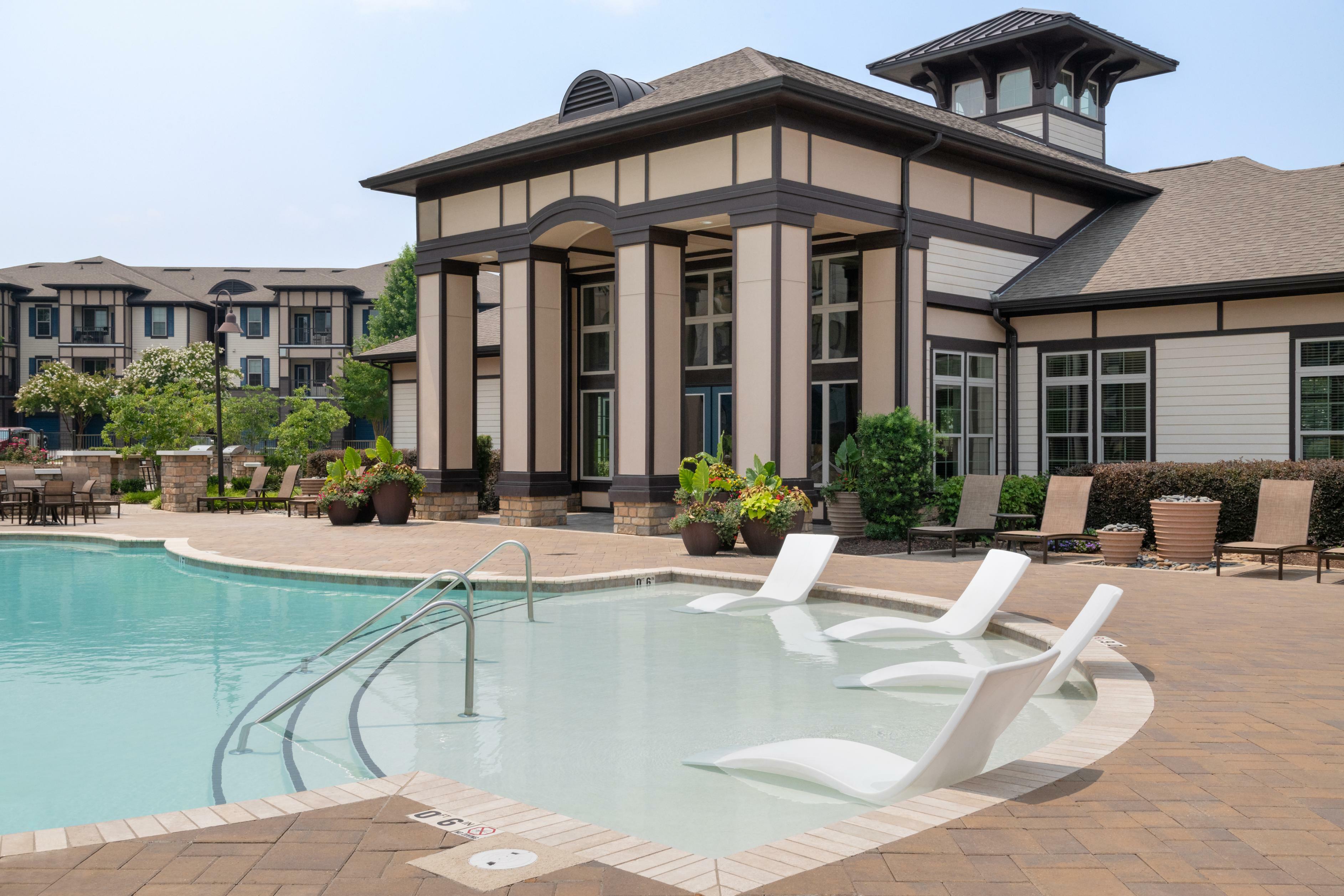 Luxurious apartment community with a stylish swimming pool, modern lounge chairs, and elegant clubhouse surrounded by landscaped greenery.