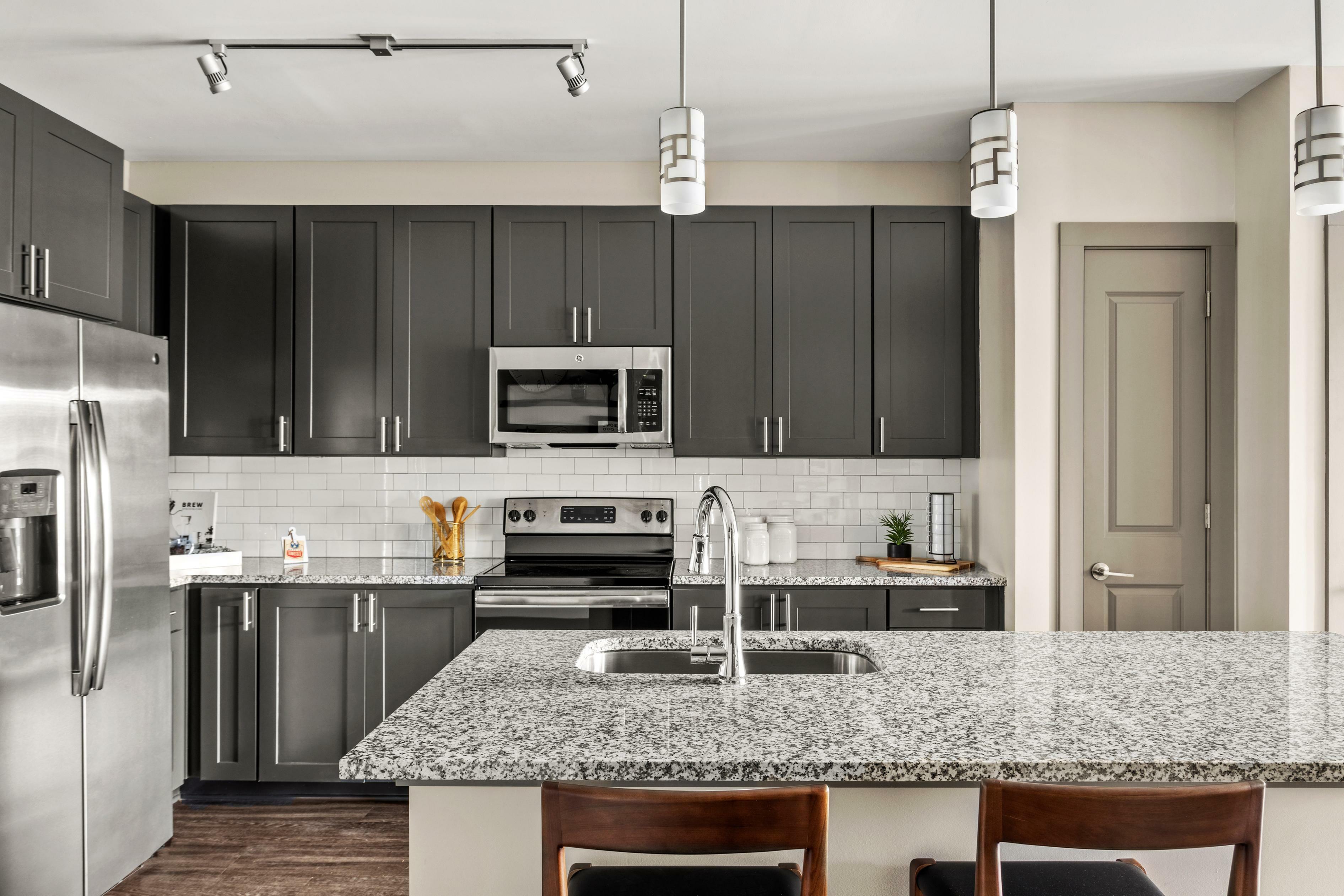 Modern kitchen with elegant gray cabinets, sleek stainless steel appliances, and a stylish granite island, creating a sophisticated culinary space.