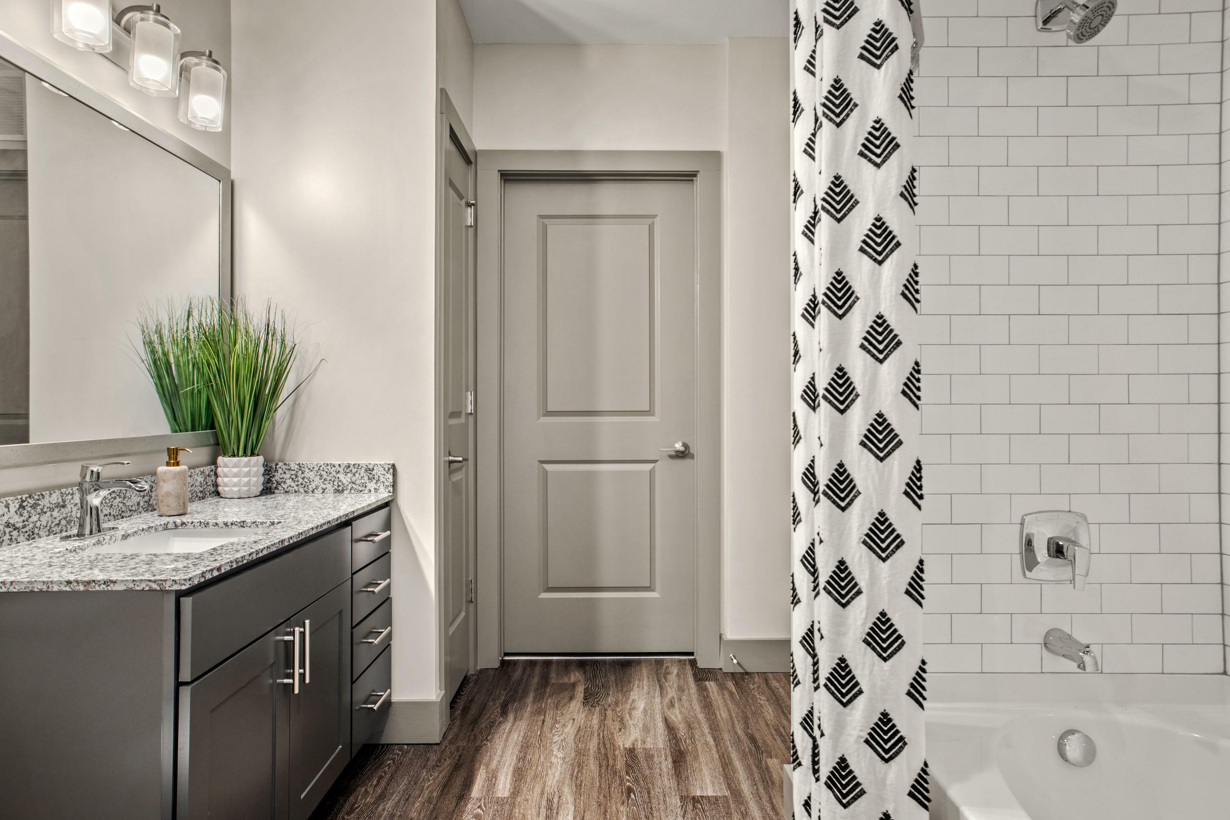Modern bathroom with sleek granite countertop, elegant dark cabinetry, and stylish tile accents, featuring a contemporary bathtub and vibrant decor.