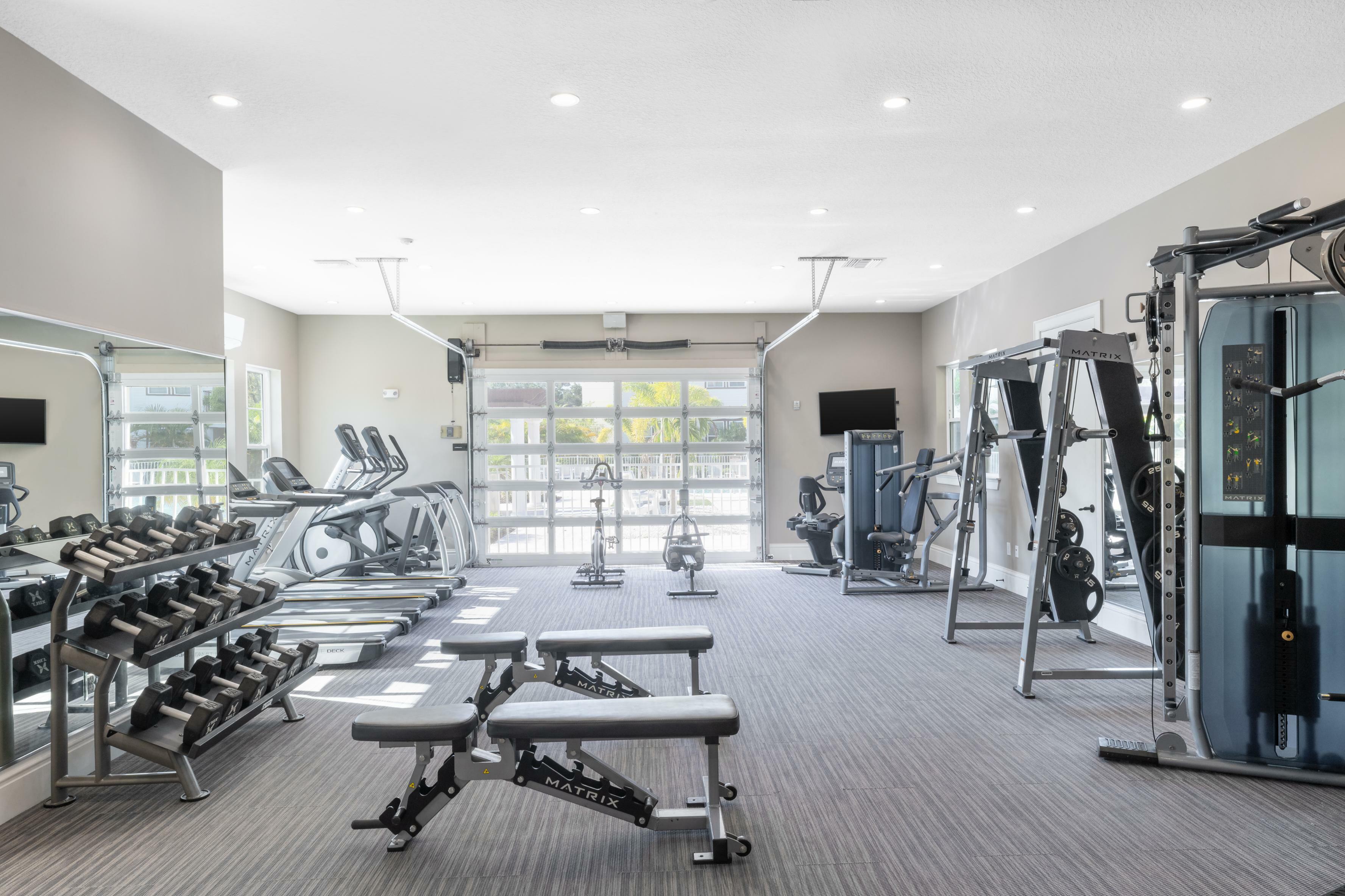 Bright and airy apartment gym with modern exercise equipment, including treadmills, weight benches, and free weights, offering a perfect space for fitness enthusiasts.