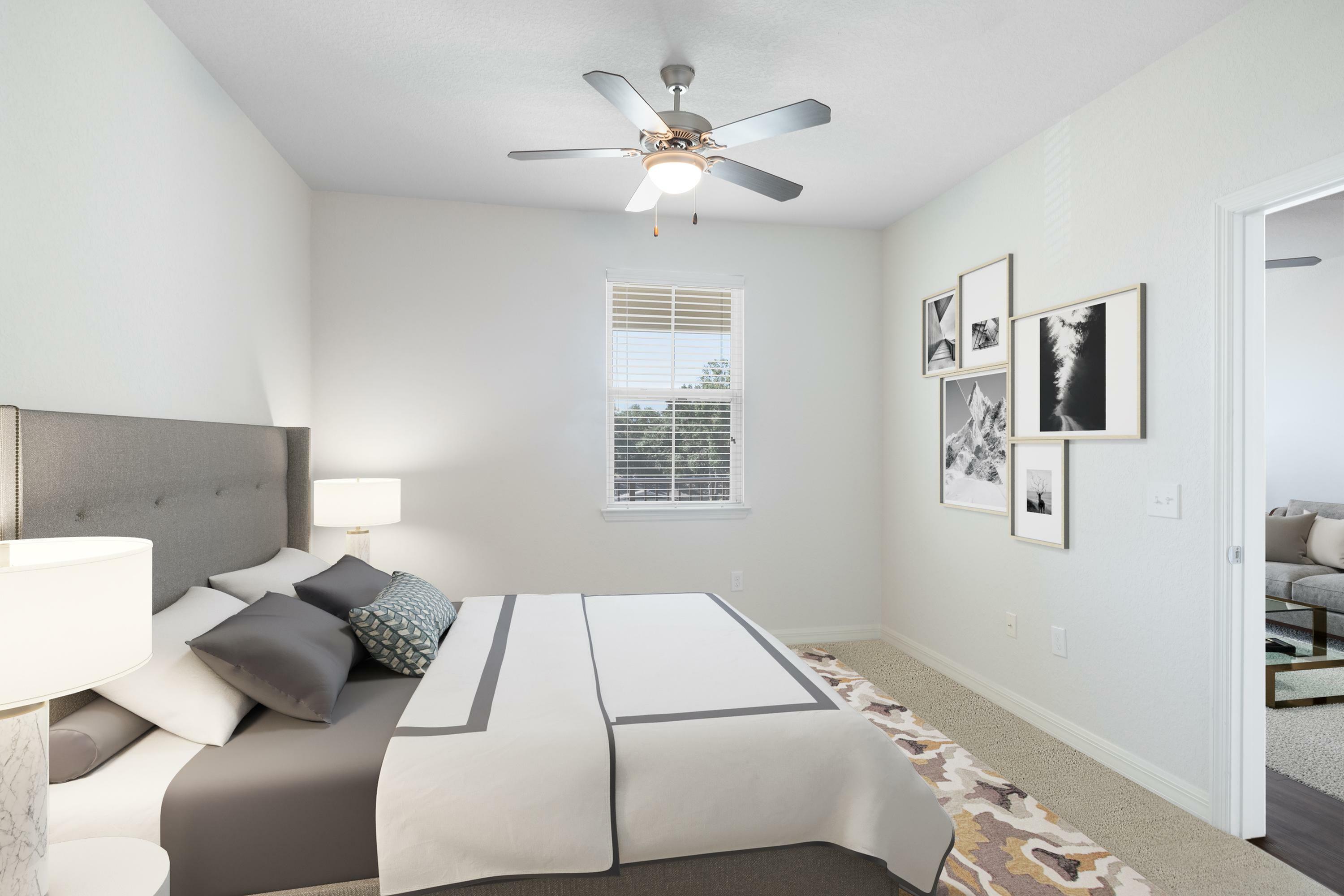 Bright bedroom with modern ceiling fan, stylish gray and white bedding, and artistic gallery wall. Natural light flows through large window, complementing the elegant decor.
