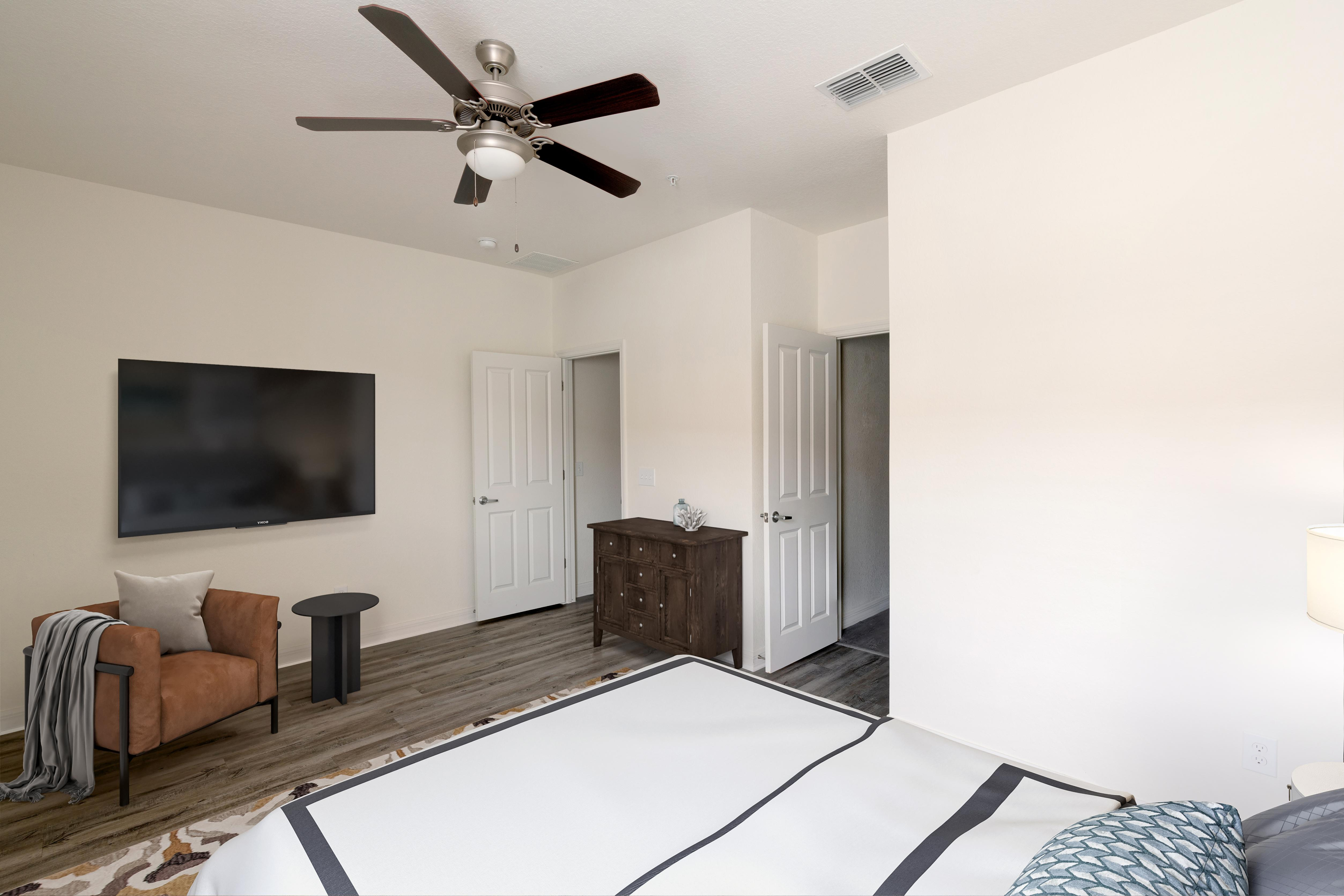 Elegant bedroom featuring a mounted flat-screen TV, plush armchair, and modern ceiling fan with sleek wood flooring.