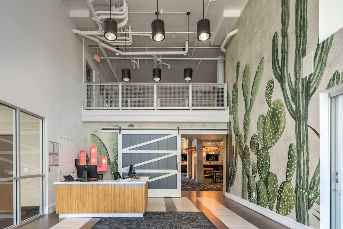 Front entrance of the building with a desk and cactus wall mural