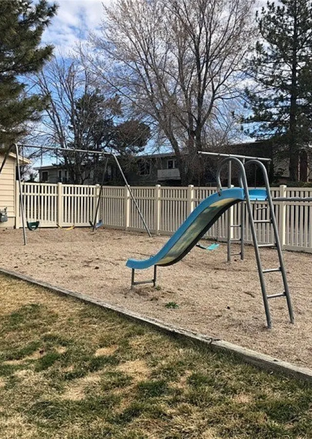 Fenced playground with a green slide and swing set at Braewood in Murray, UT