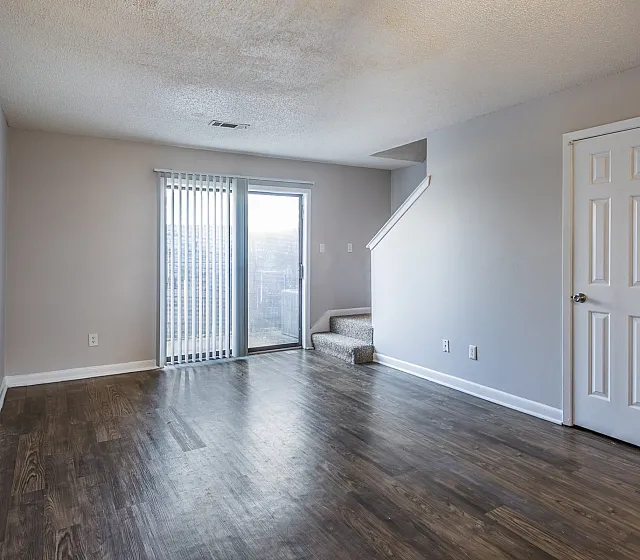 Living room with patio doors and wood-style floors at Collier Village Apartments in Collierville, TN