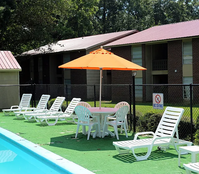Poolside seating with shade umbrellas at Meadow Creek Apartments in Jackson, MS