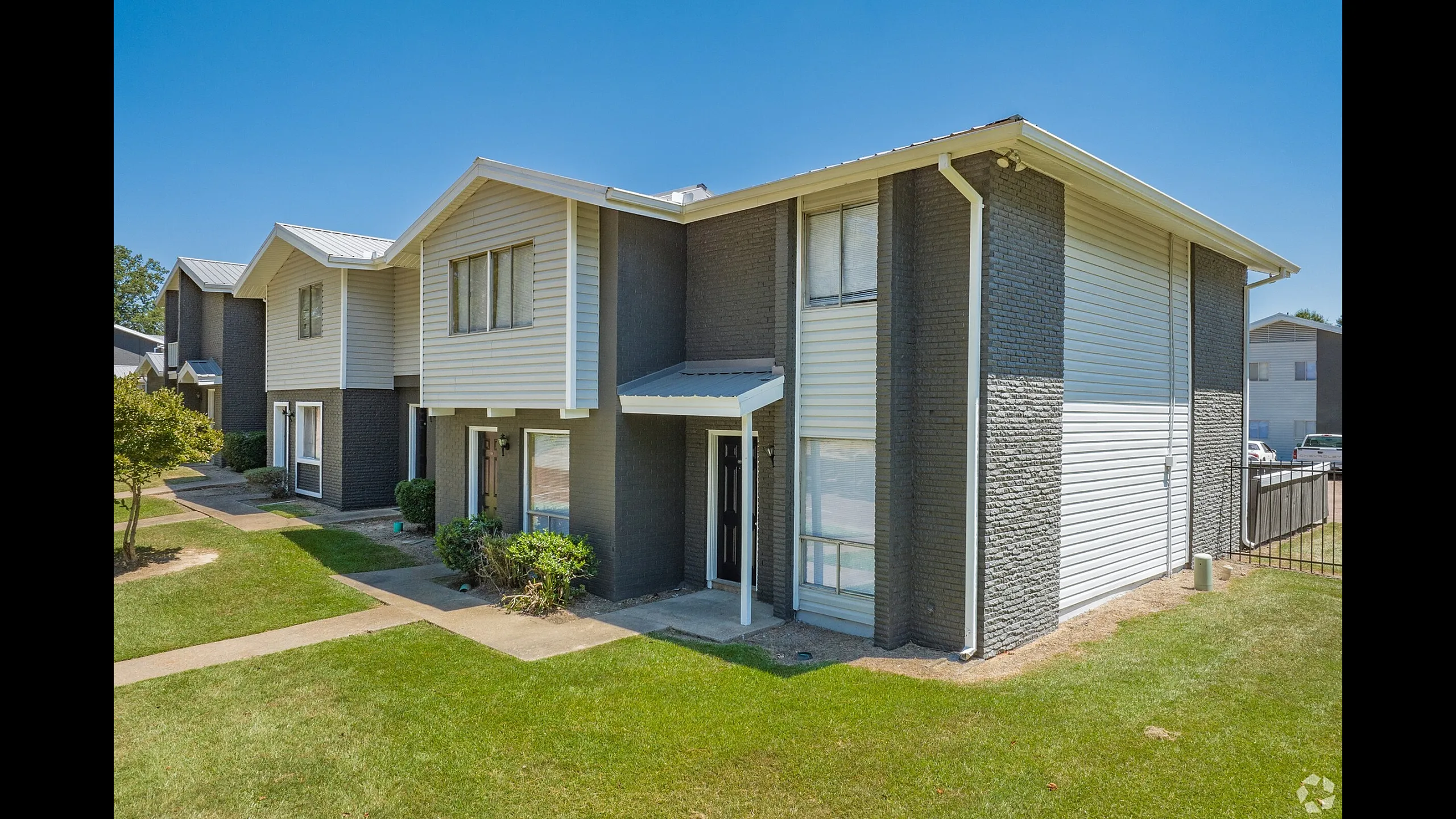 Two-story gray townhome building with a green lawn at Pines Apartments in Jackson, MS