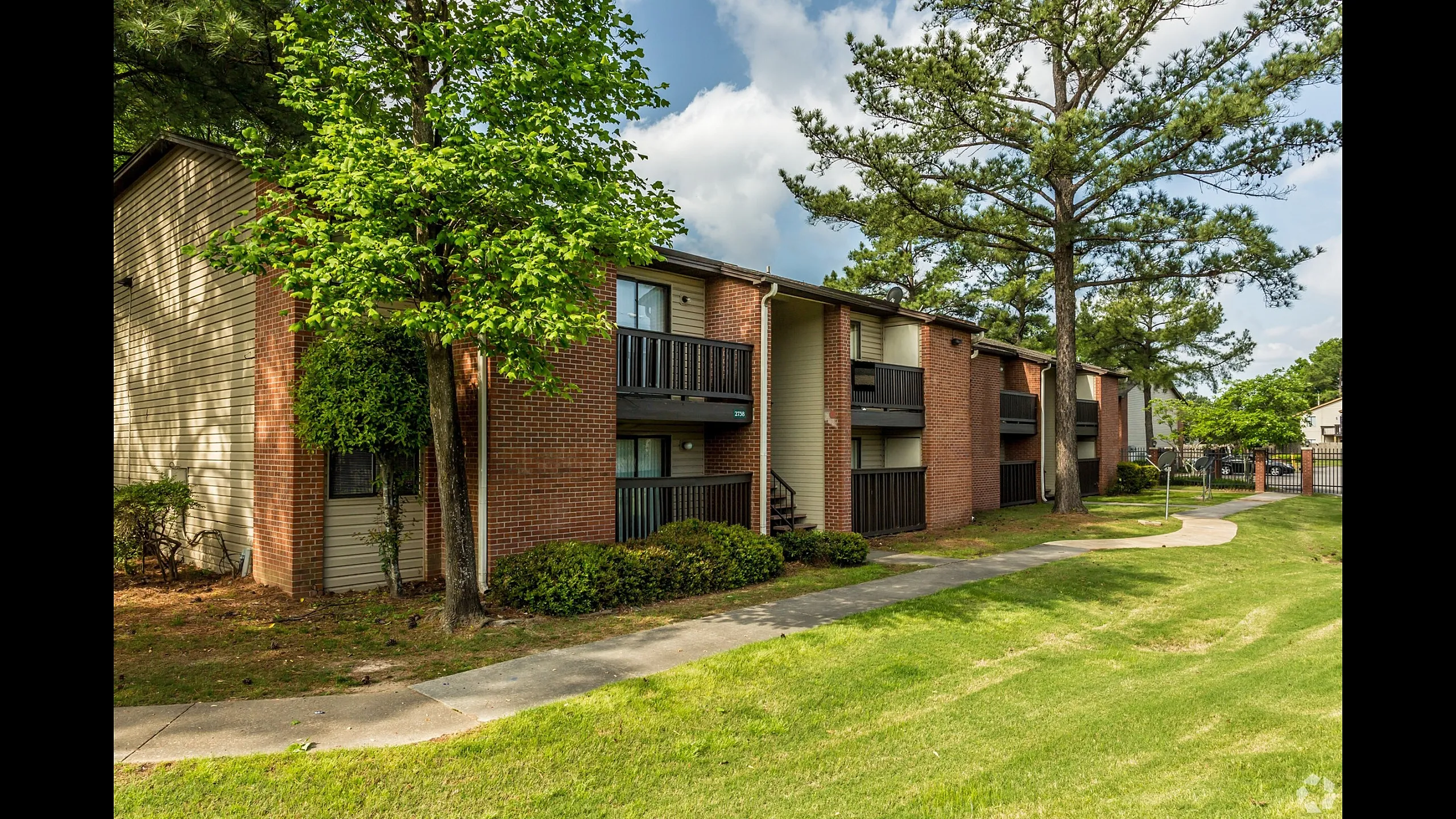 Brick buildings with balconies framed by shade trees at Hickory Pointe in Memphis, TN