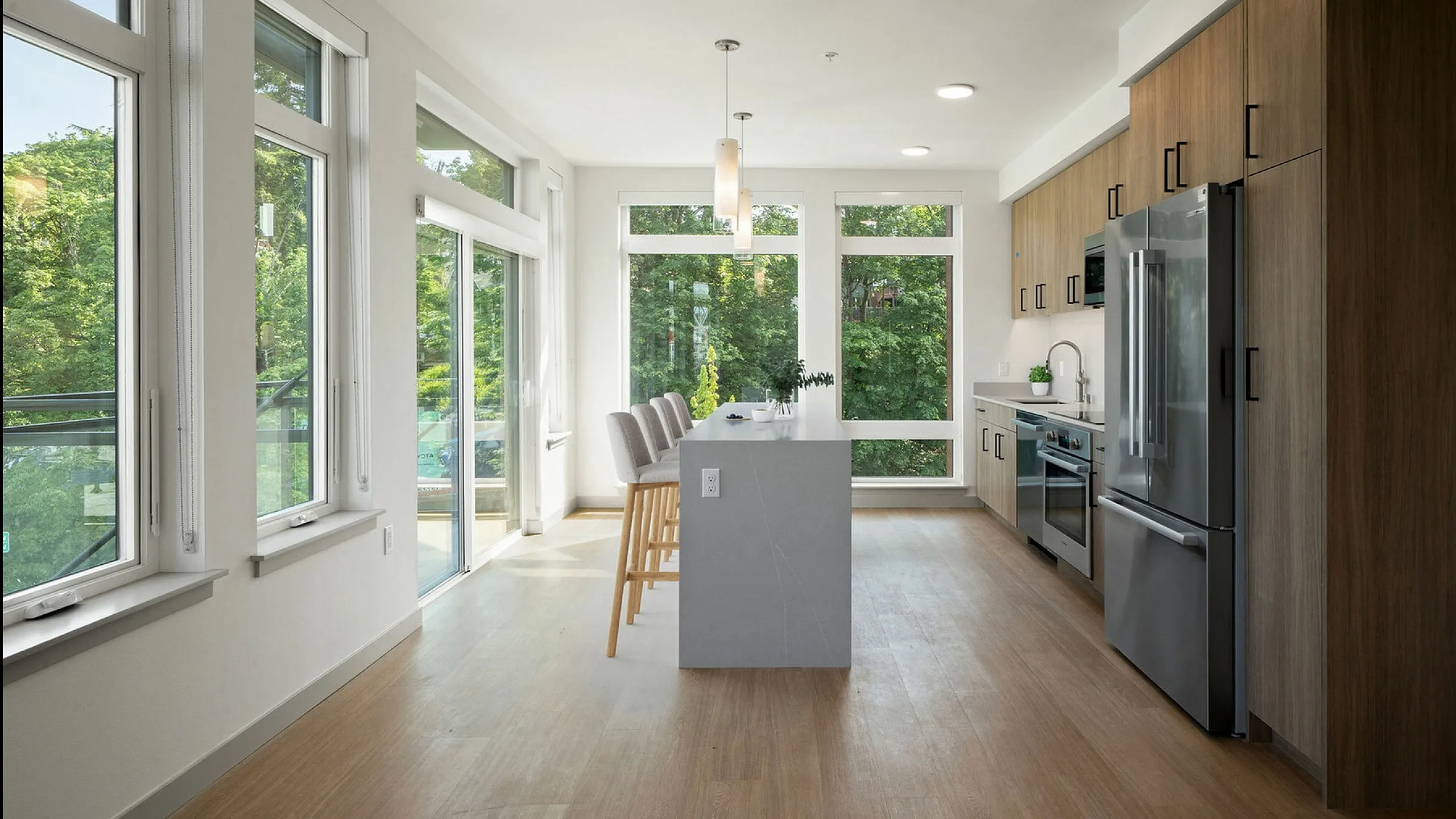 Bright and modern kitchen with sleek appliances, large windows offering lush green views, and a chic breakfast bar with seating.